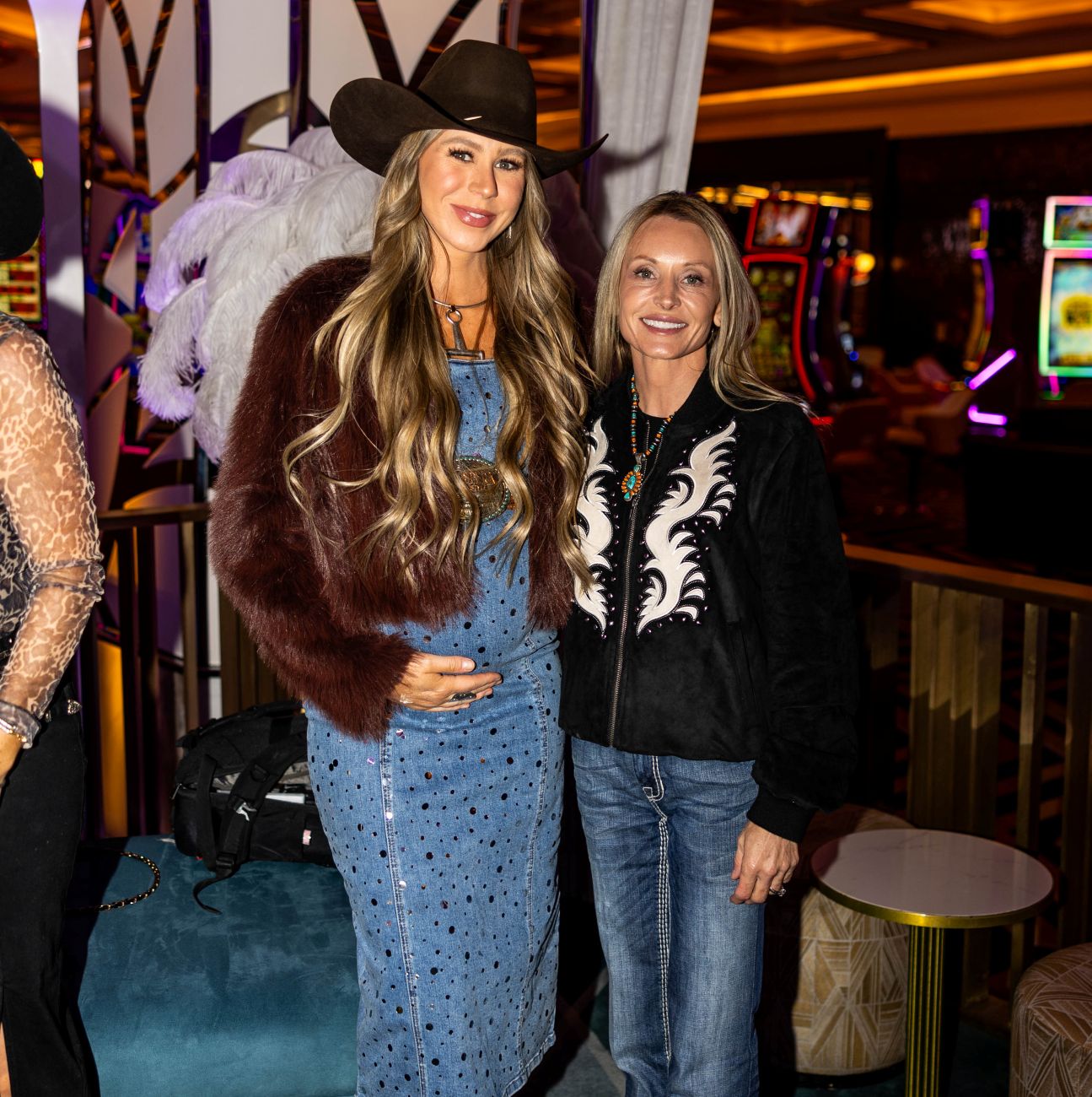 Two women posing together in a casino setting with slot machines in the background.