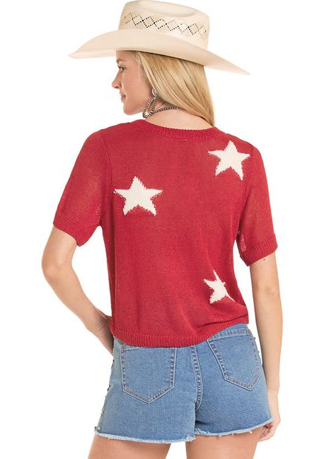 Person wearing a red t-shirt with white stars, blue shorts, and white cowboy boots on a white background