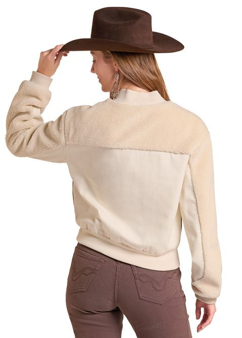 A woman shown from the back wearing a cream and brown western-style jacket, brown pants, and a brown cowboy hat, set against a plain white background.