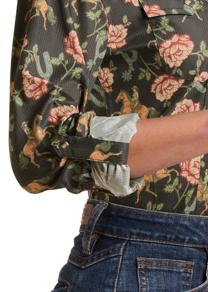 Close-up of a person wearing a dark floral and animal print button-up shirt with rolled sleeves and blue jeans, shown against a white background.