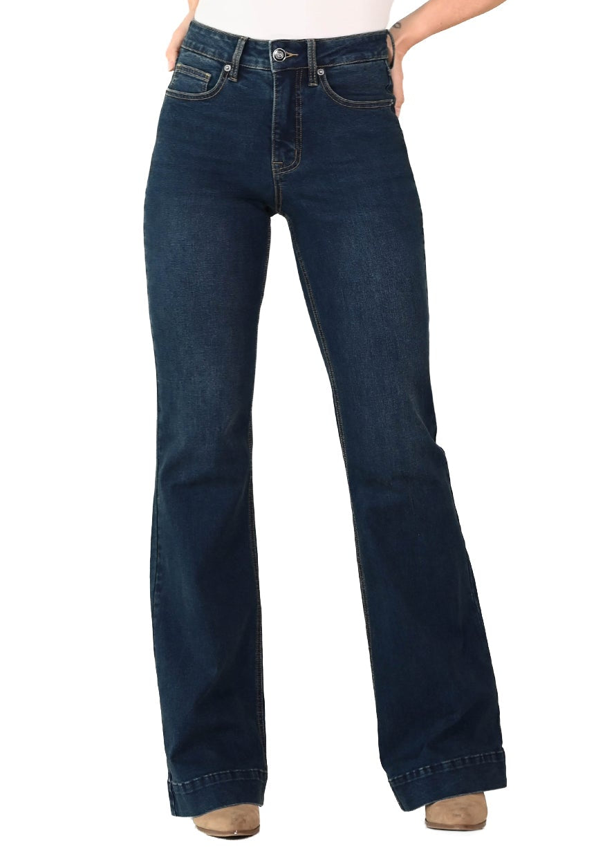 A woman modeling dark blue high-waisted flare jeans with a white sleeveless top and a beige cowboy hat, standing against a plain white background.