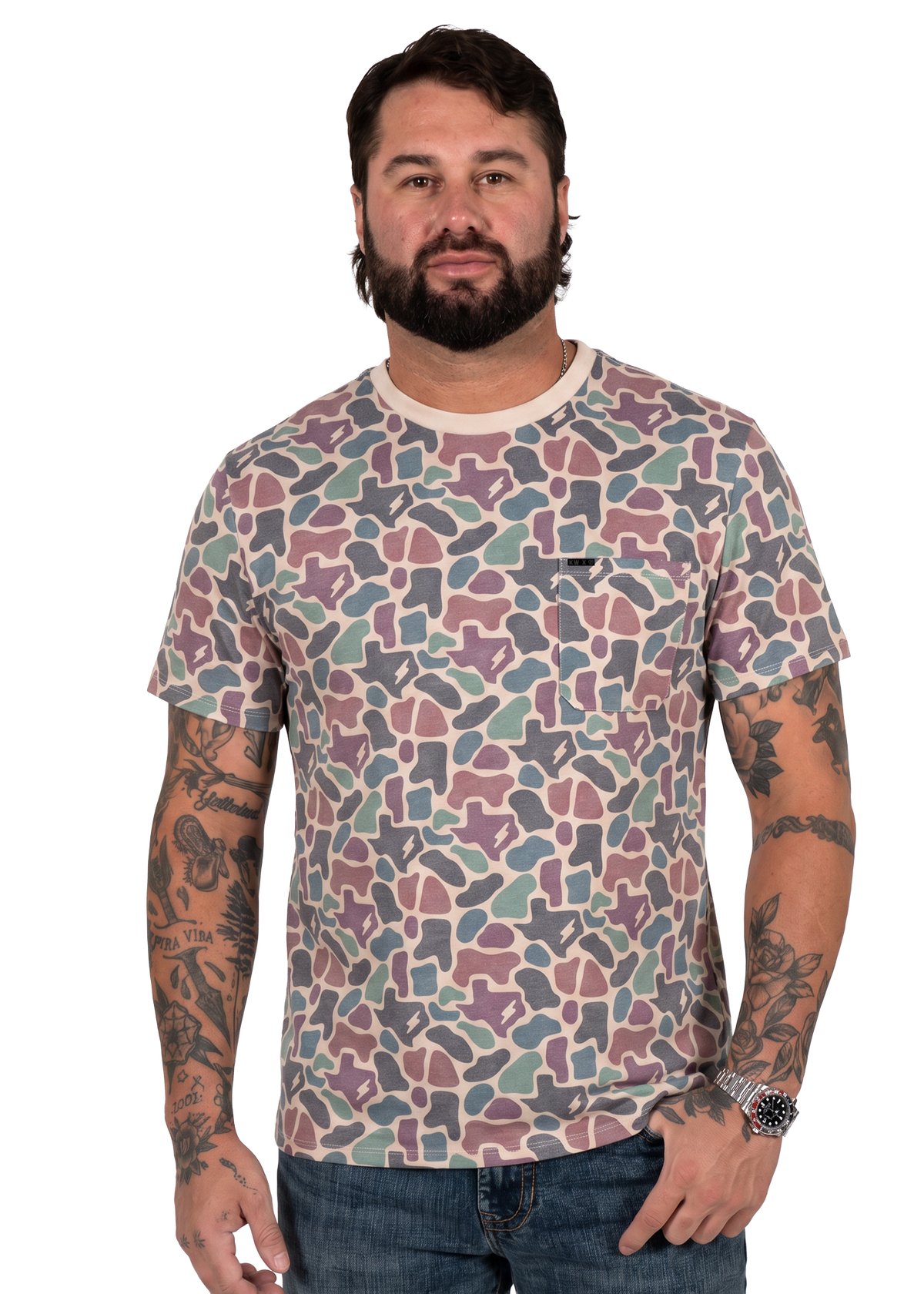 A man wearing a short-sleeve crewneck t-shirt with a multicolor abstract geometric pattern in dusty pink, teal, and gray, paired with blue jeans against a plain white background.
