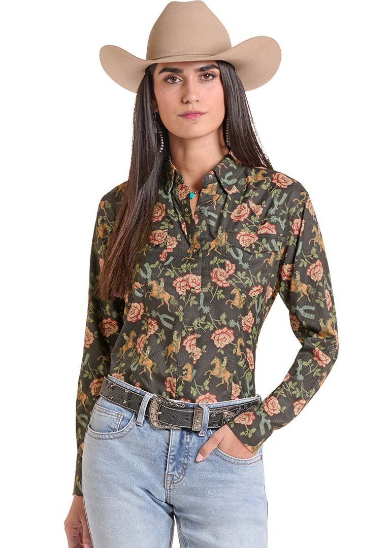 A woman modeling a long-sleeve western-style button-up shirt with a dark olive green base and a pink and orange floral print, paired with a tan cowboy hat and light blue jeans against a white background.