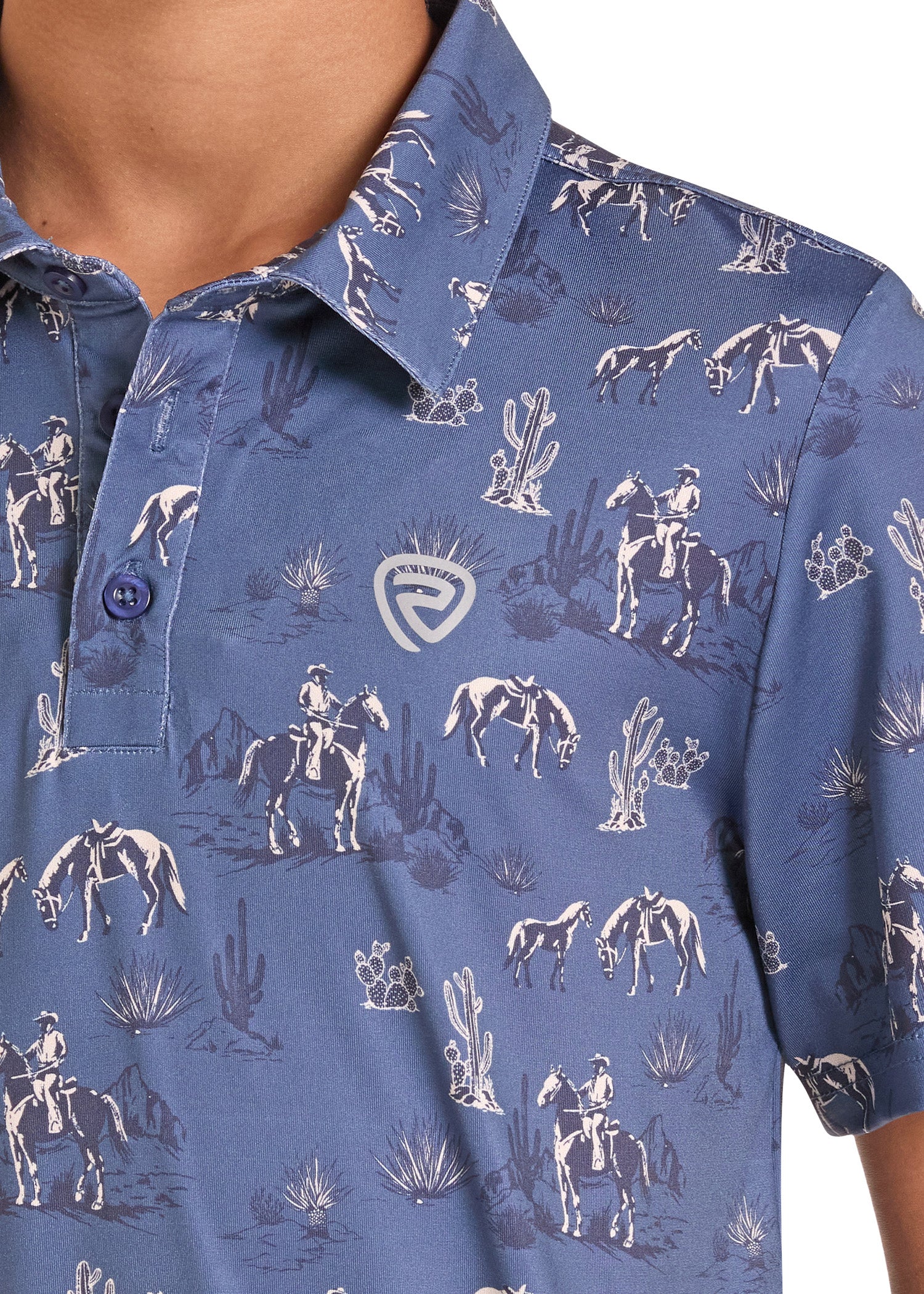 Close-up of a blue short-sleeve polo shirt with a white desert cowboy print, featuring riders on horseback and cacti, with a shield logo on the chest.