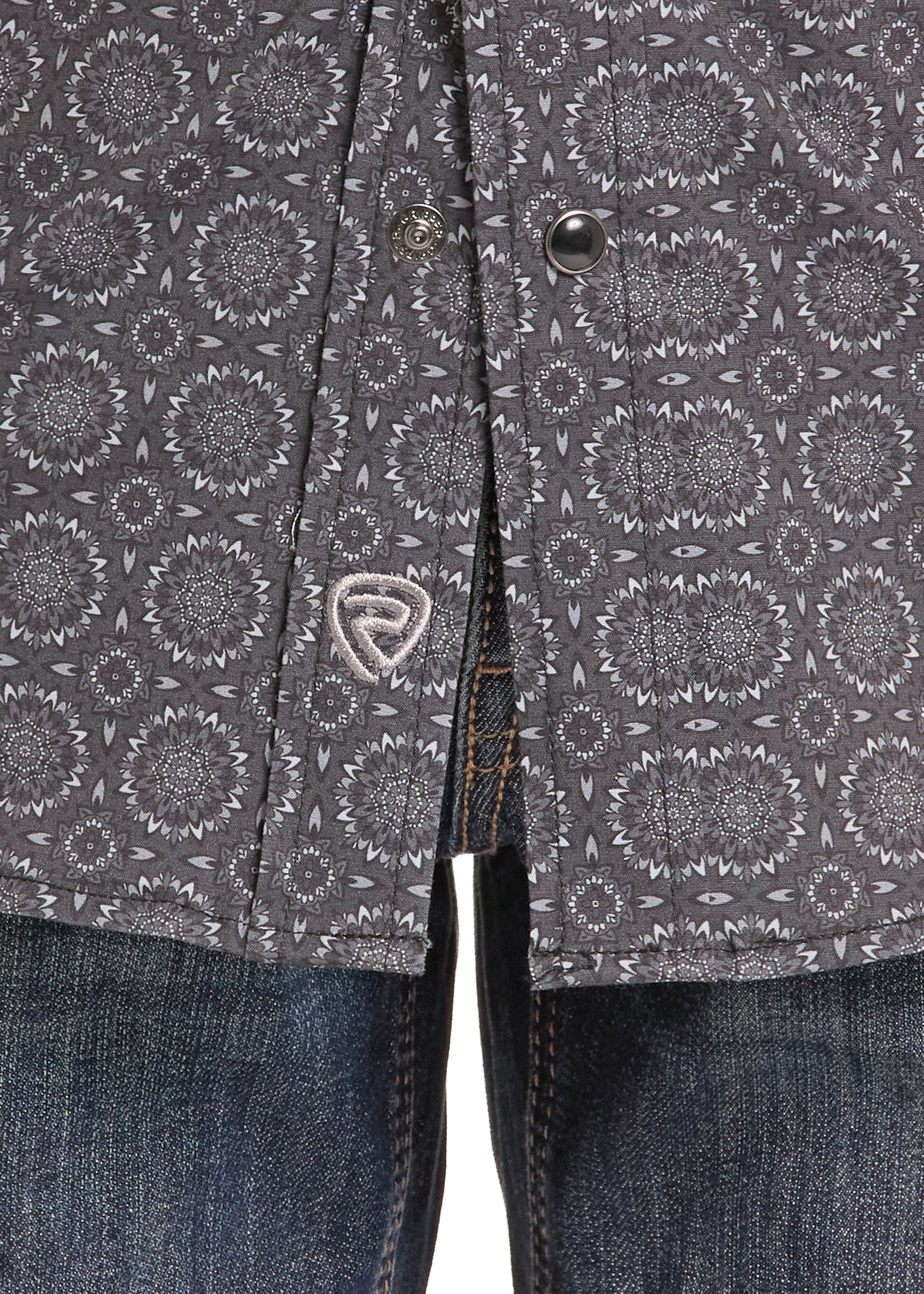 Close-up of a dark gray patterned button-up shirt with a small shield logo patch on the chest, paired with blue jeans.