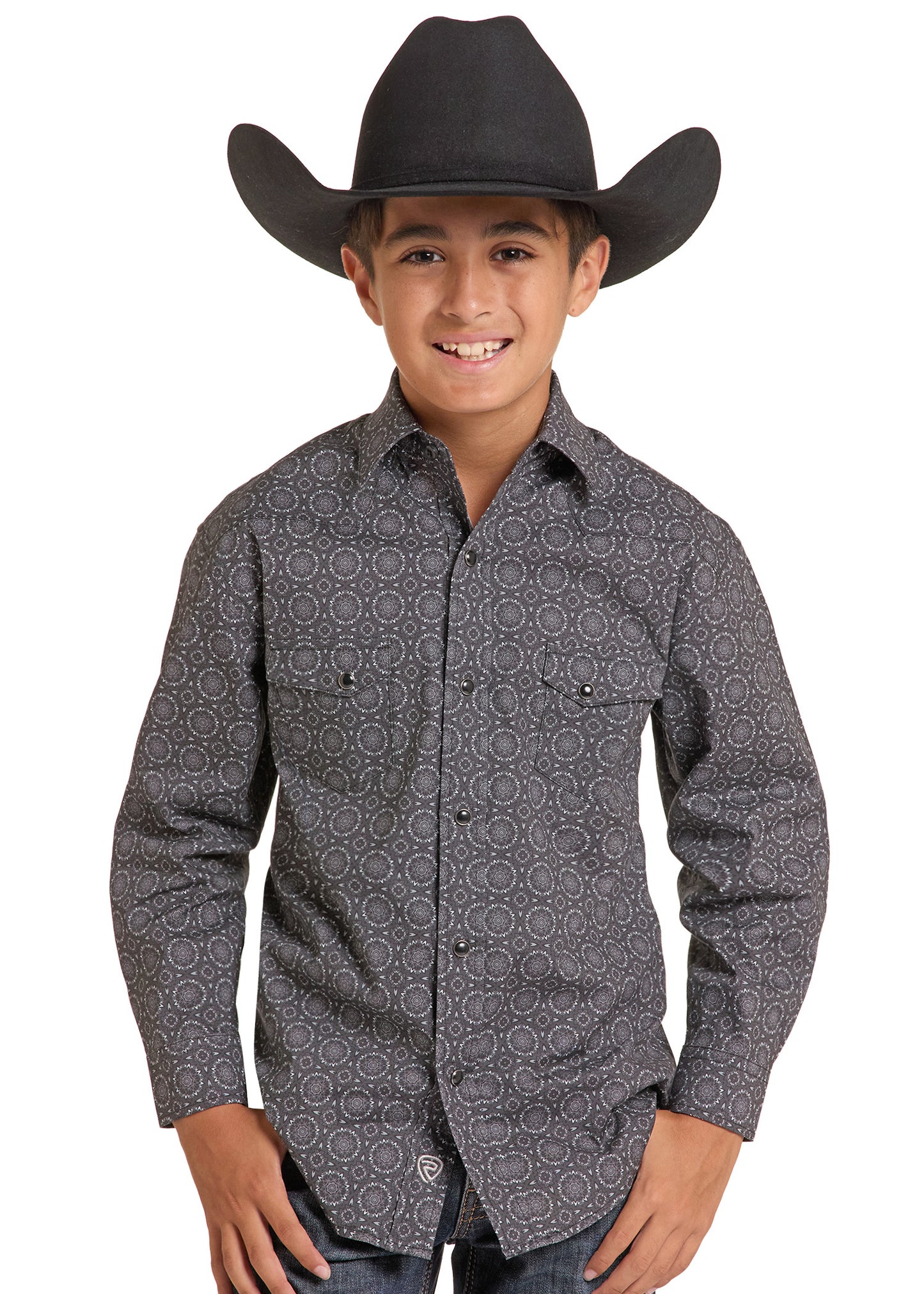 A young boy wearing a black cowboy hat and a dark gray long-sleeve western shirt with a circular geometric pattern, standing against a white background.