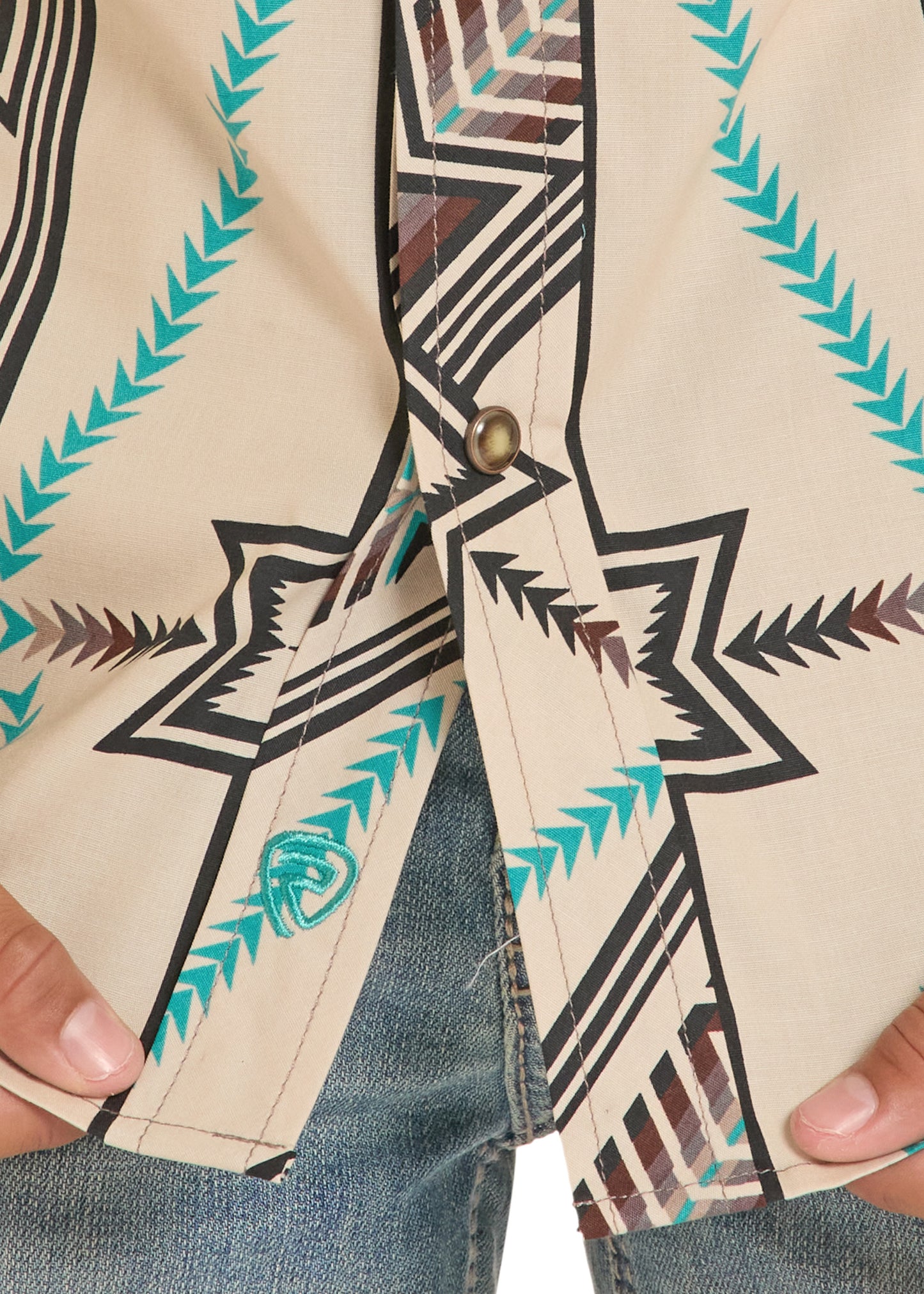 Close-up of a person wearing a beige shirt with tribal pattern, holding it open.