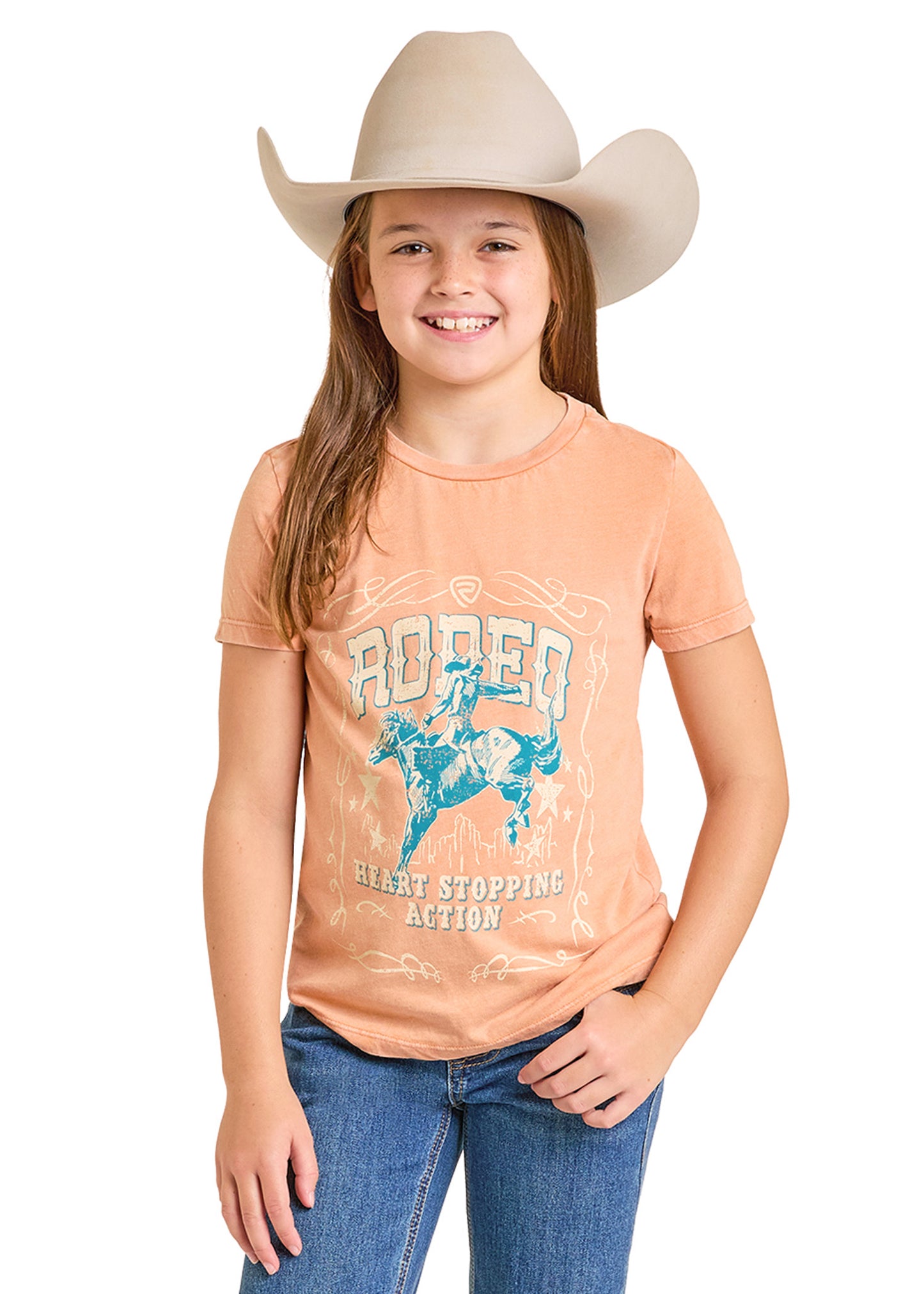 Young girl wearing a peach t-shirt with a graphic design and a cowboy hat on a white background