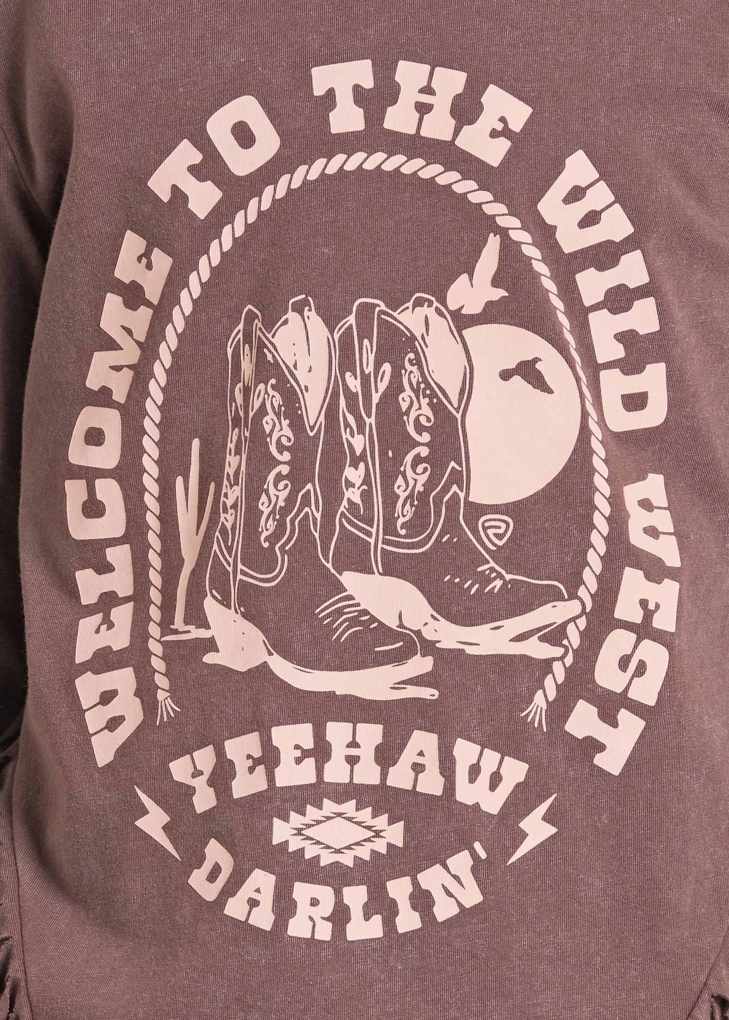 Close-up of a heathered brownish-purple graphic t-shirt featuring a western design with cowboy boots, a moon, and the text 'WELCOME TO THE WILD WEST' and 'YEEHAW DARLIN''.