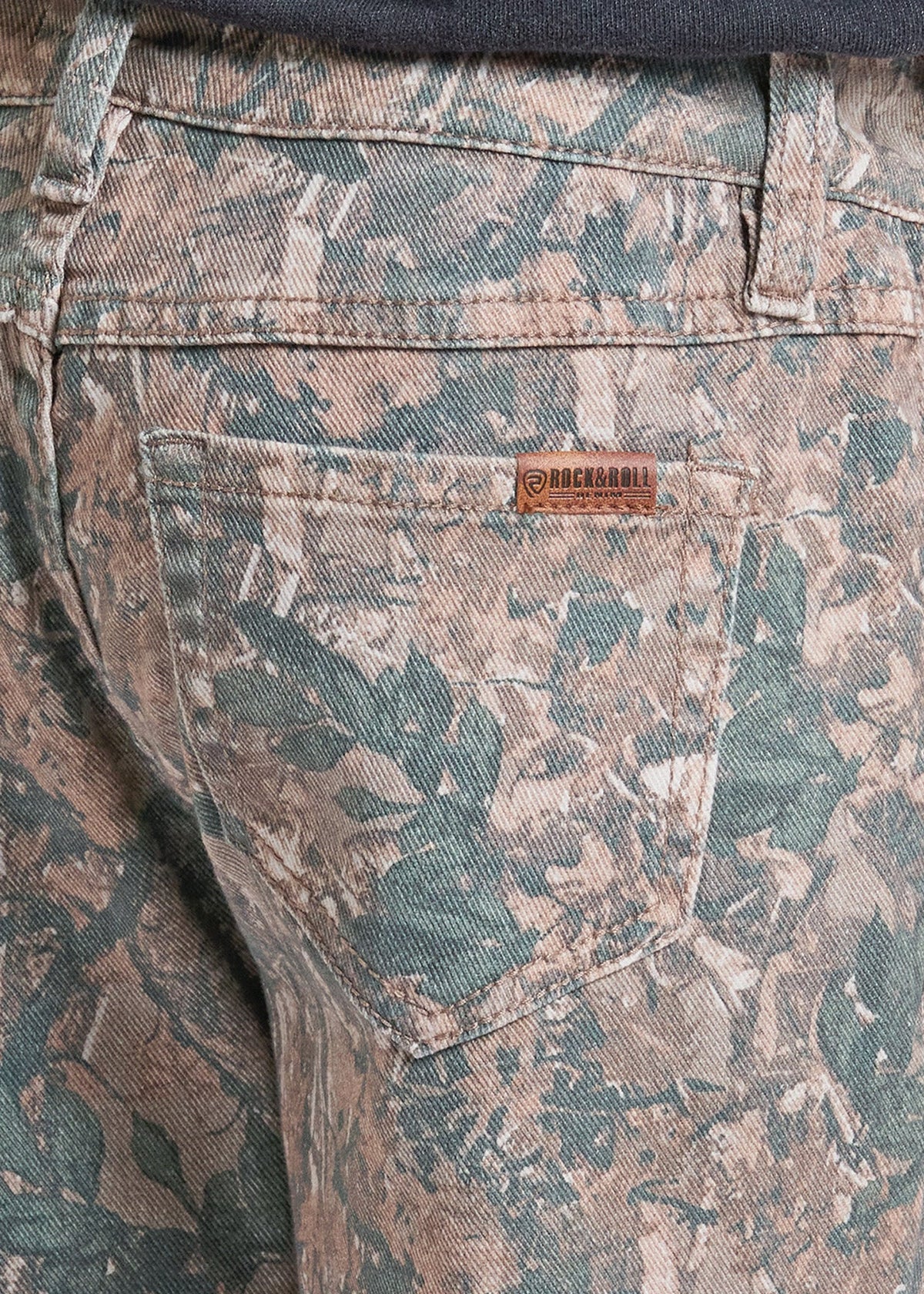 Close-up of the back waistband and pocket area of camouflage-patterned denim jeans, showing a small brown leather brand patch on the pocket.