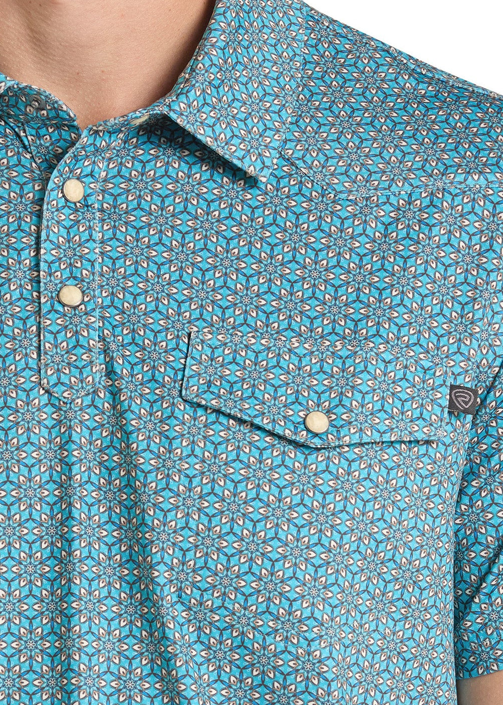 Close-up of a man wearing a short-sleeve button-up shirt with a blue, teal, and gray geometric pattern. The shirt features a collar, a two-button placket, and a chest pocket with a snap closure.