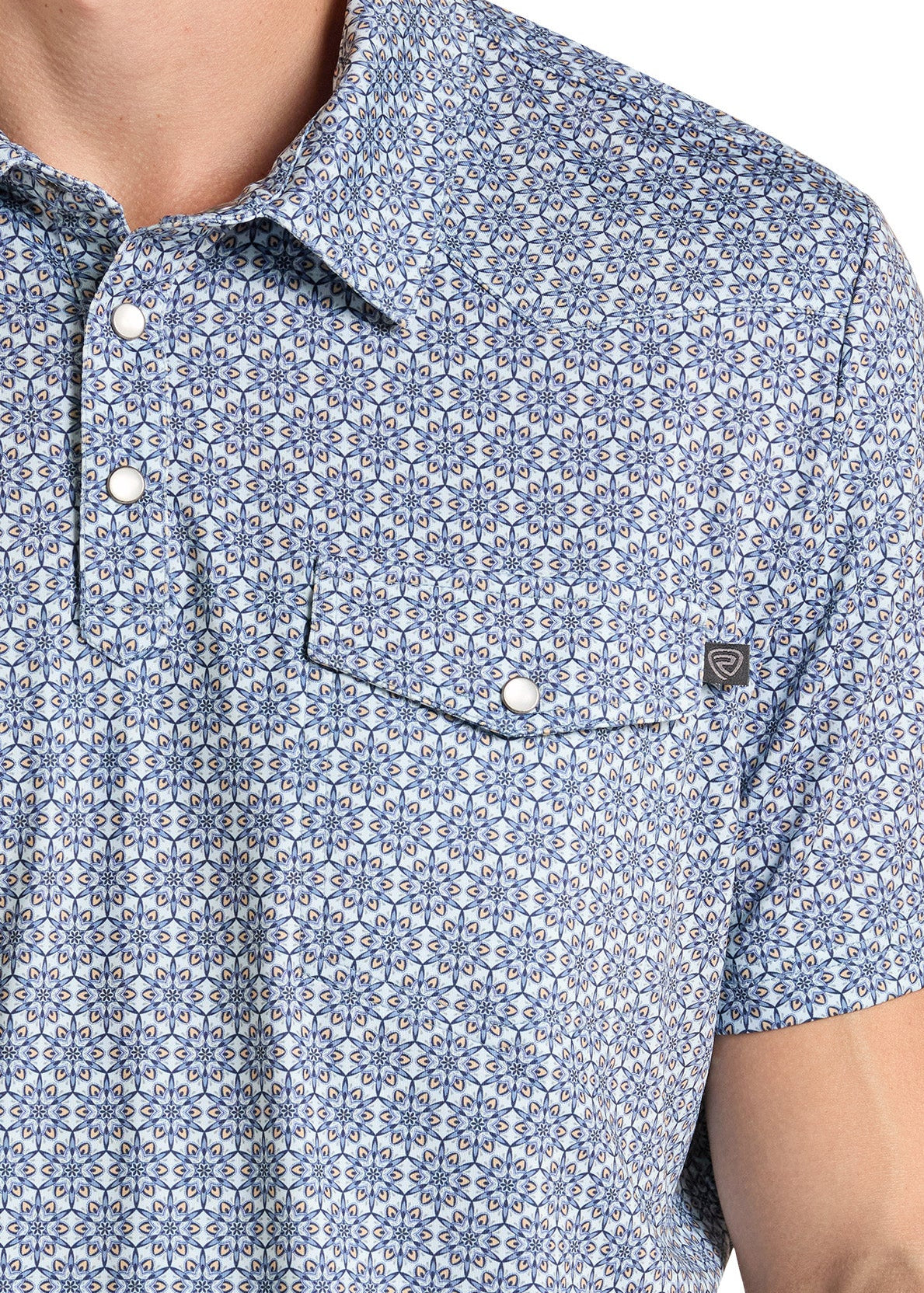Close-up of a man wearing a short-sleeve button-up shirt with a blue and white geometric pattern, featuring a chest pocket with a snap closure and a small brand tag.