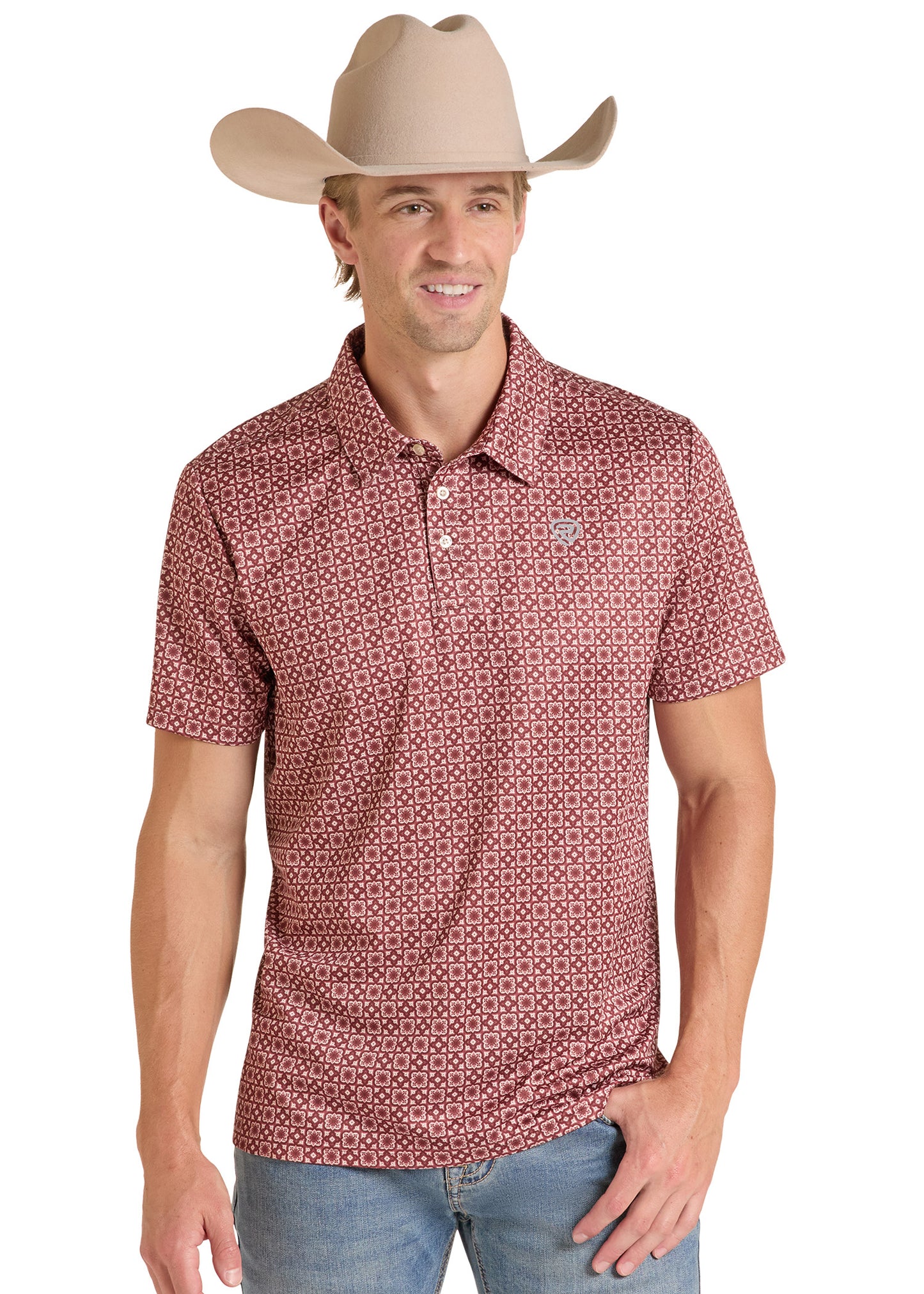 A man wearing a short-sleeve polo shirt with a small geometric pattern in red and white, paired with a beige cowboy hat and blue jeans, against a plain white background.