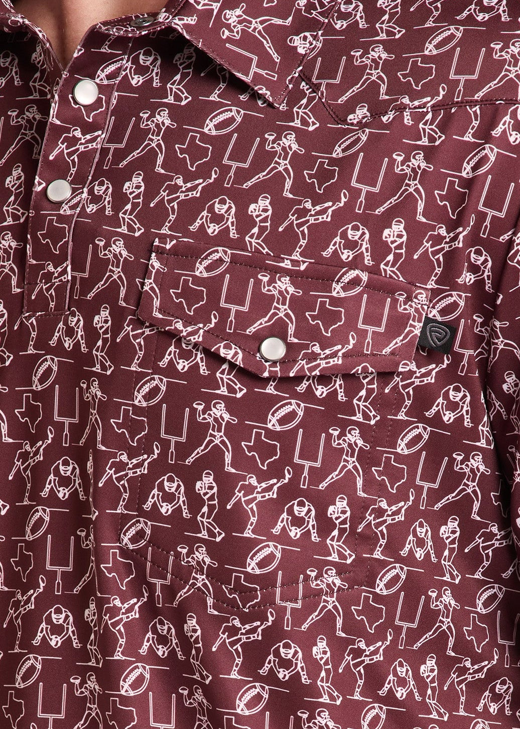 A close-up of a man wearing a short-sleeve button-up shirt in burgundy with a white cartoon-style graphic pattern. The shirt features a chest pocket with a button and a small black brand tab.