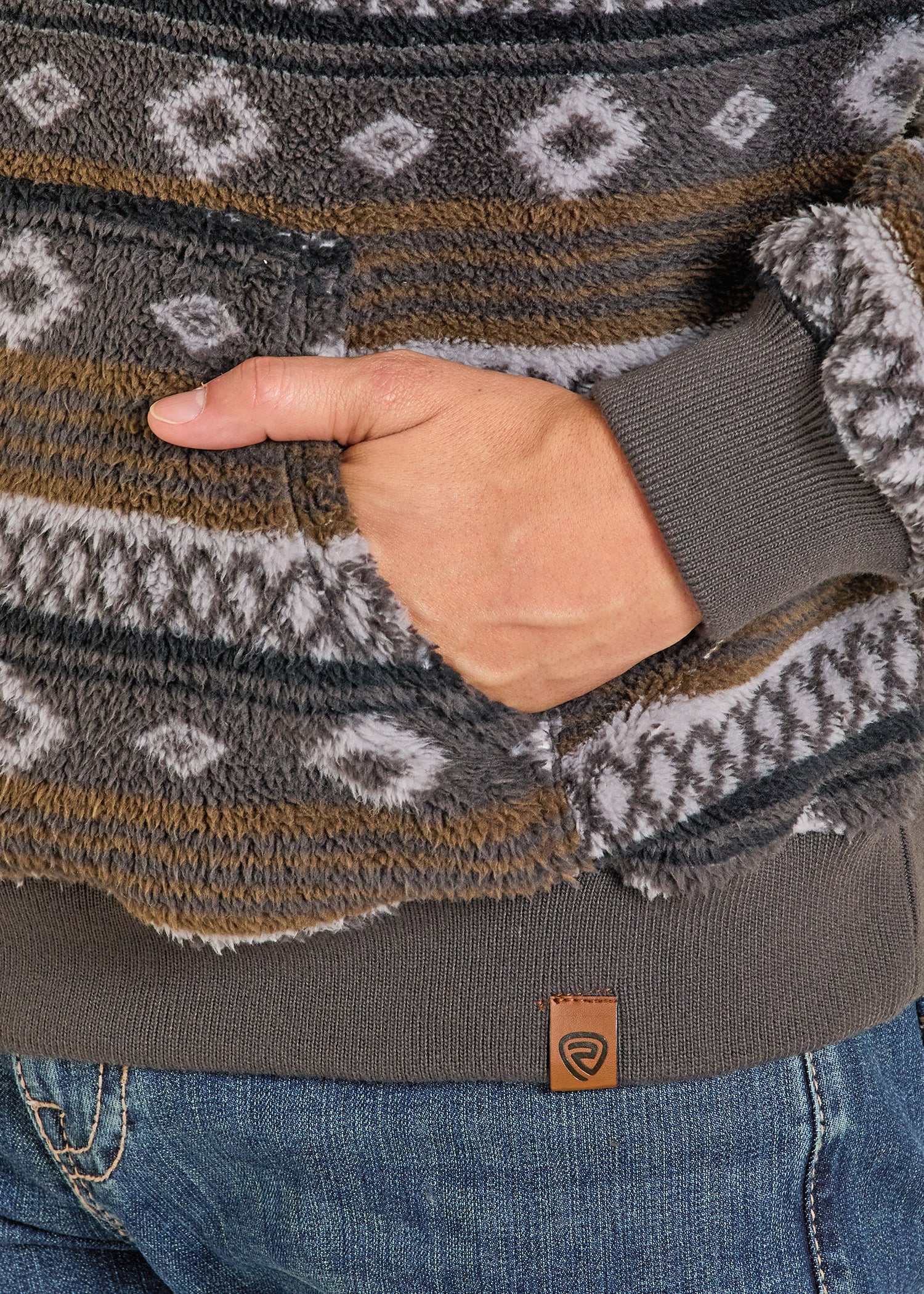 Close-up of a person wearing a patterned sweater with a hand in the pocket, showing a brand logo.