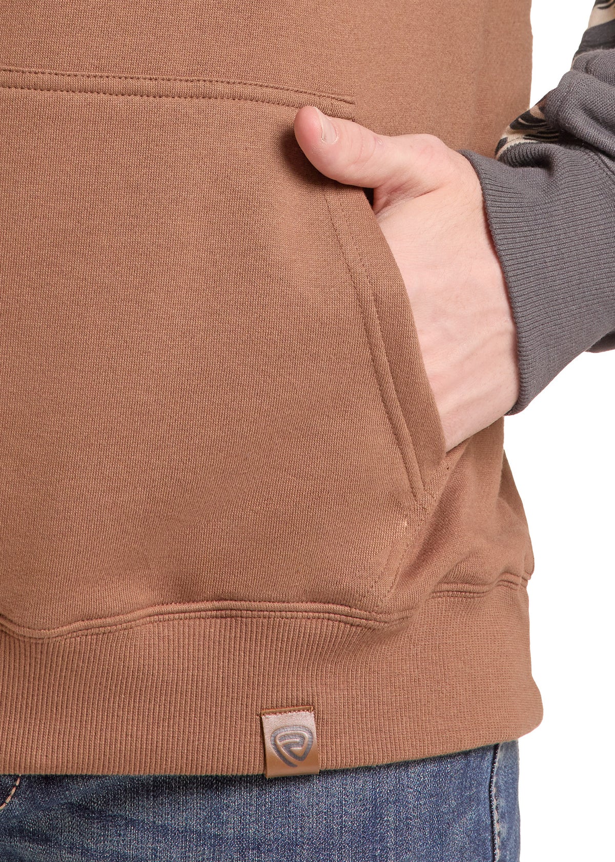 Close-up of a person wearing a brown fleece hoodie with a side pocket, their hand in the pocket, and a small brand tag near the hem.
