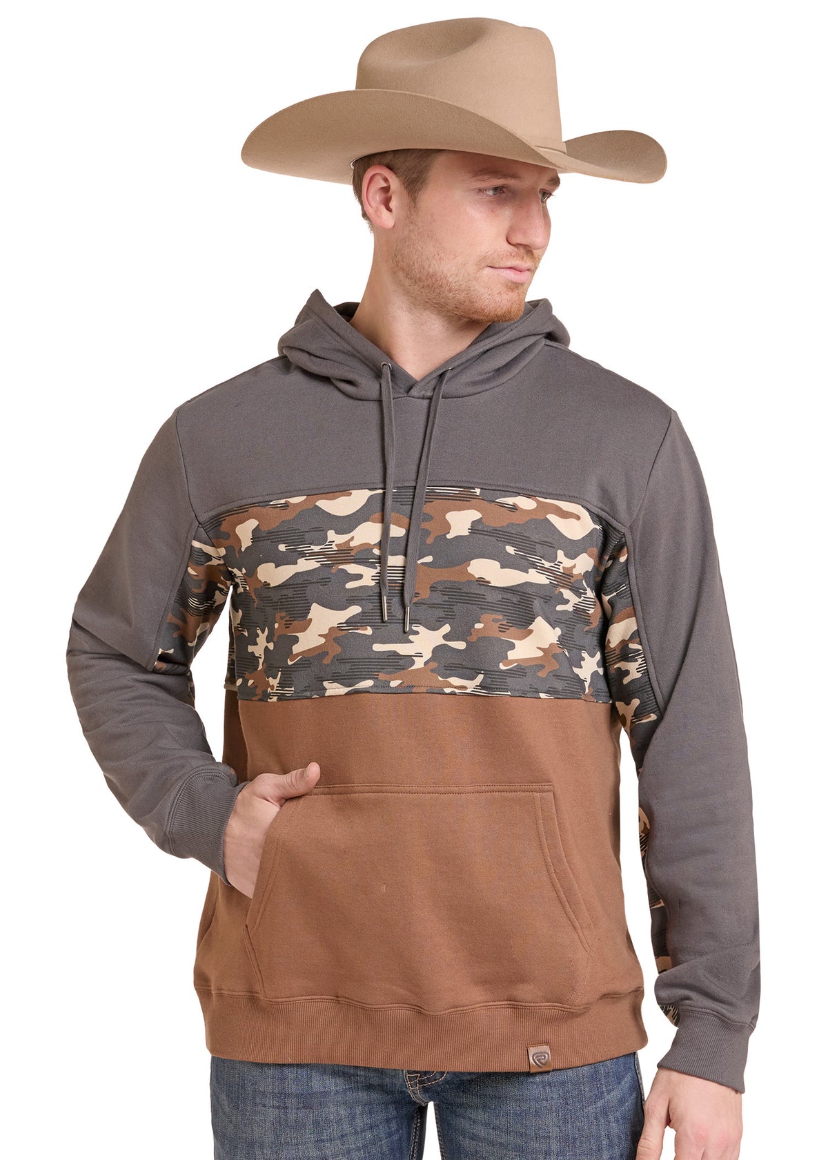 A man wearing a color-blocked pullover hoodie with a brown and gray design and a camouflage pattern across the chest, paired with a tan cowboy hat and blue jeans, against a plain white background.