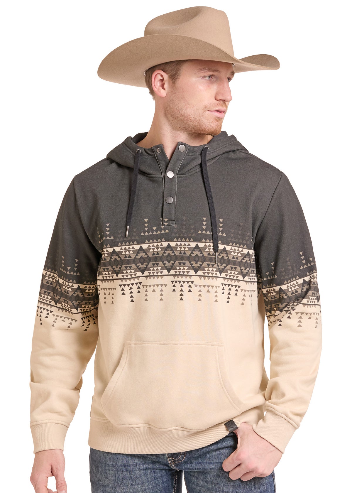 A man wearing a dark charcoal and beige pullover hoodie with a geometric pattern across the chest and sleeves, paired with a tan cowboy hat and blue jeans, against a plain white background.