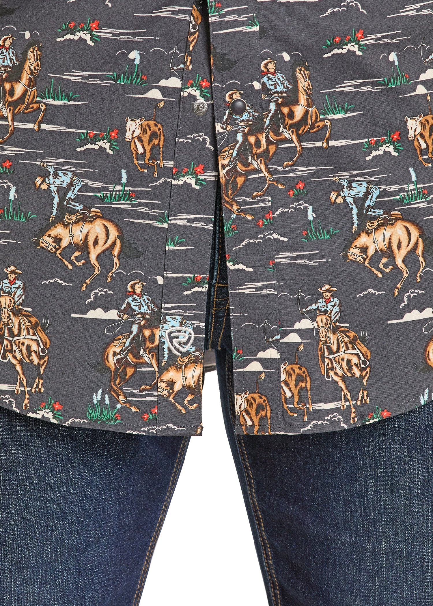 Close-up of a shirt with a cowboy pattern featuring horses, cowboys, and cows on a dark background.
