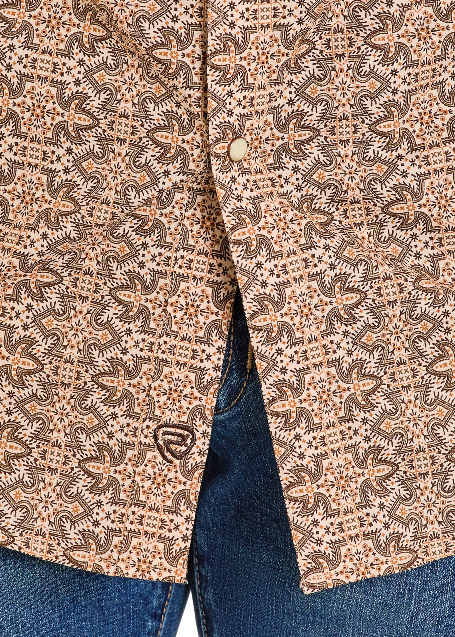 Close-up of a patterned jacket with a button and blue jeans underneath.
