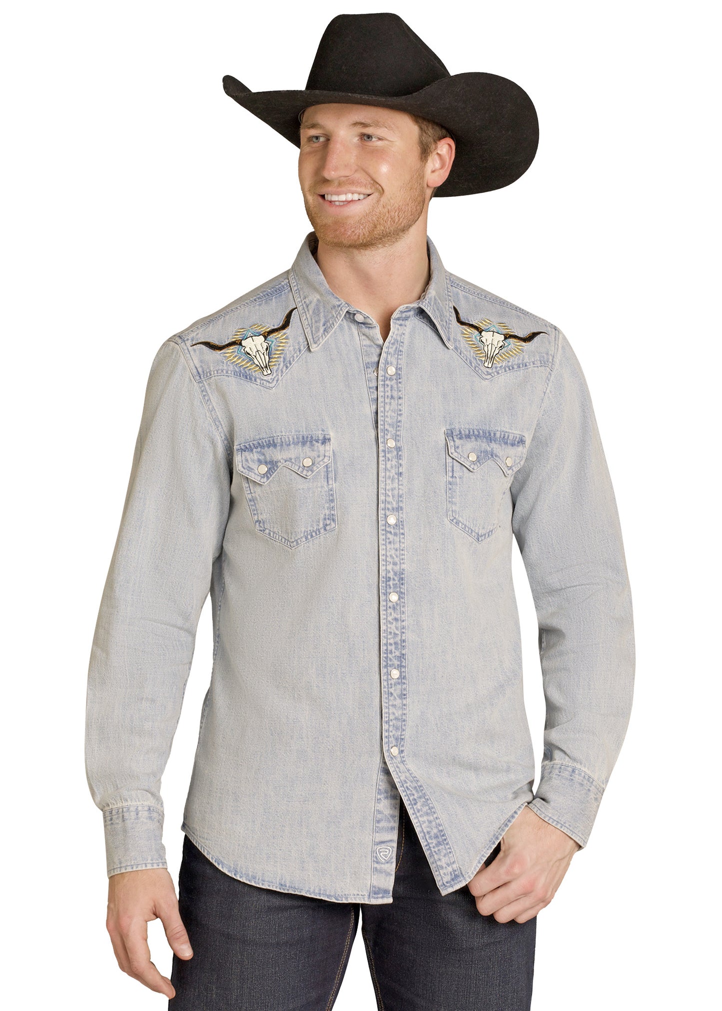Man wearing a light gray denim shirt with embroidered details and a black cowboy hat on a white background
