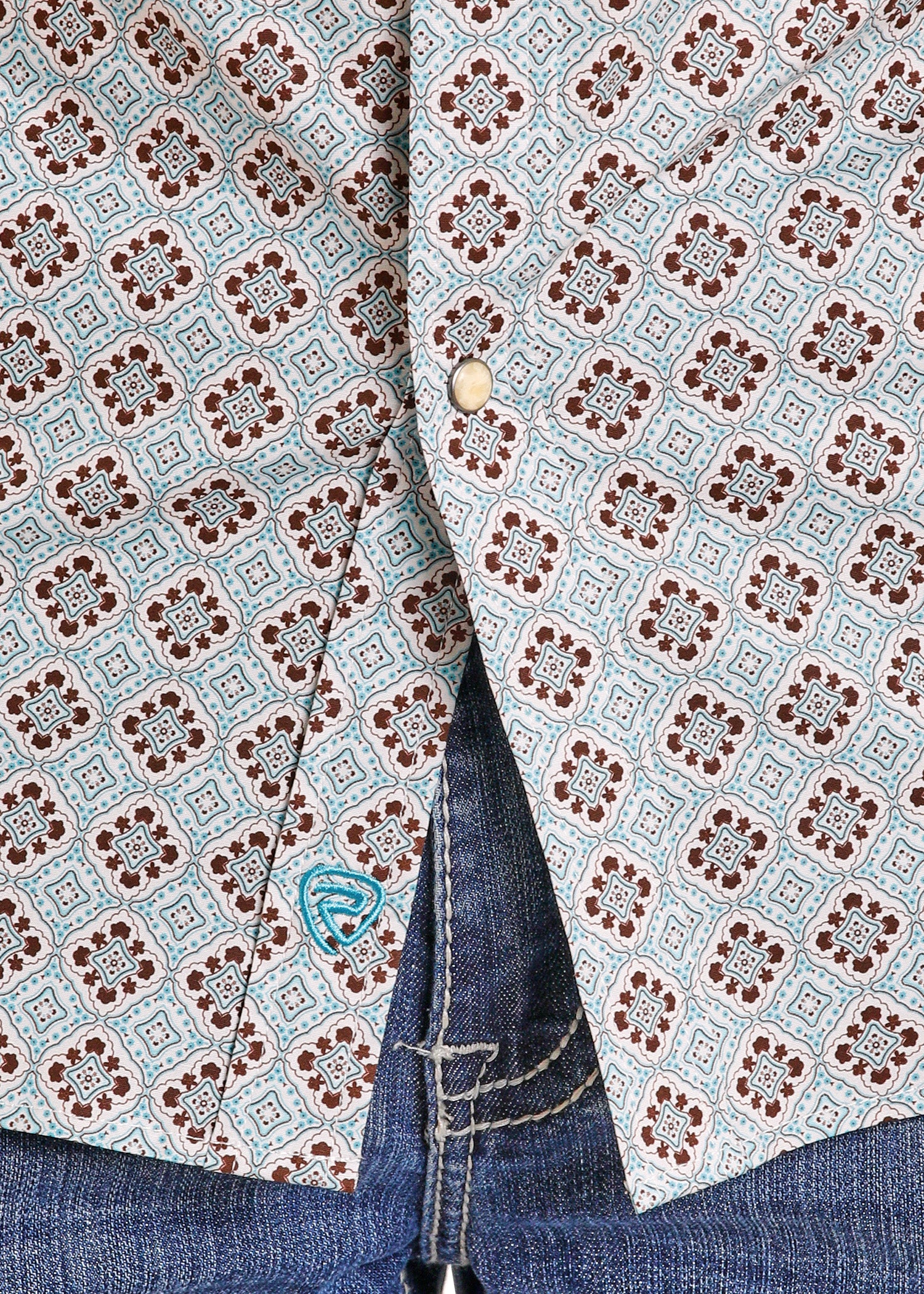 Close-up of a patterned shirt with a button and jeans.