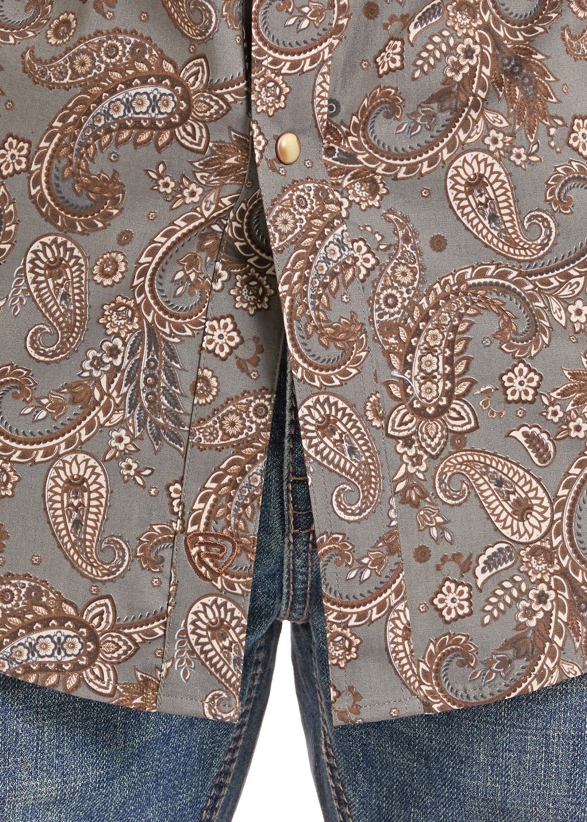 Close-up of a button-front shirt with a brown and beige paisley pattern on a taupe-gray background, worn over blue jeans.