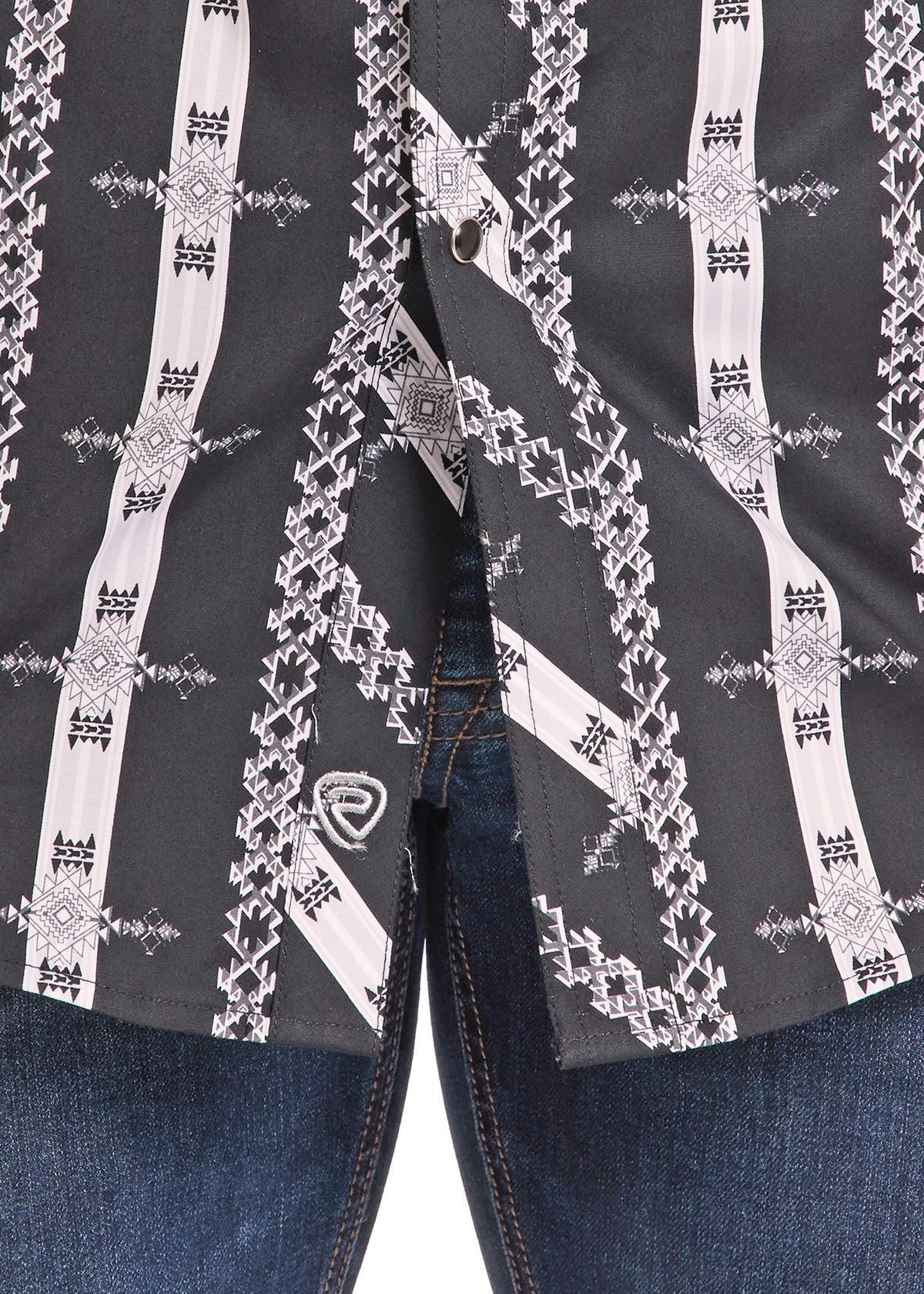 Close-up of a black western-style shirt with white geometric patterns, worn open over blue jeans.