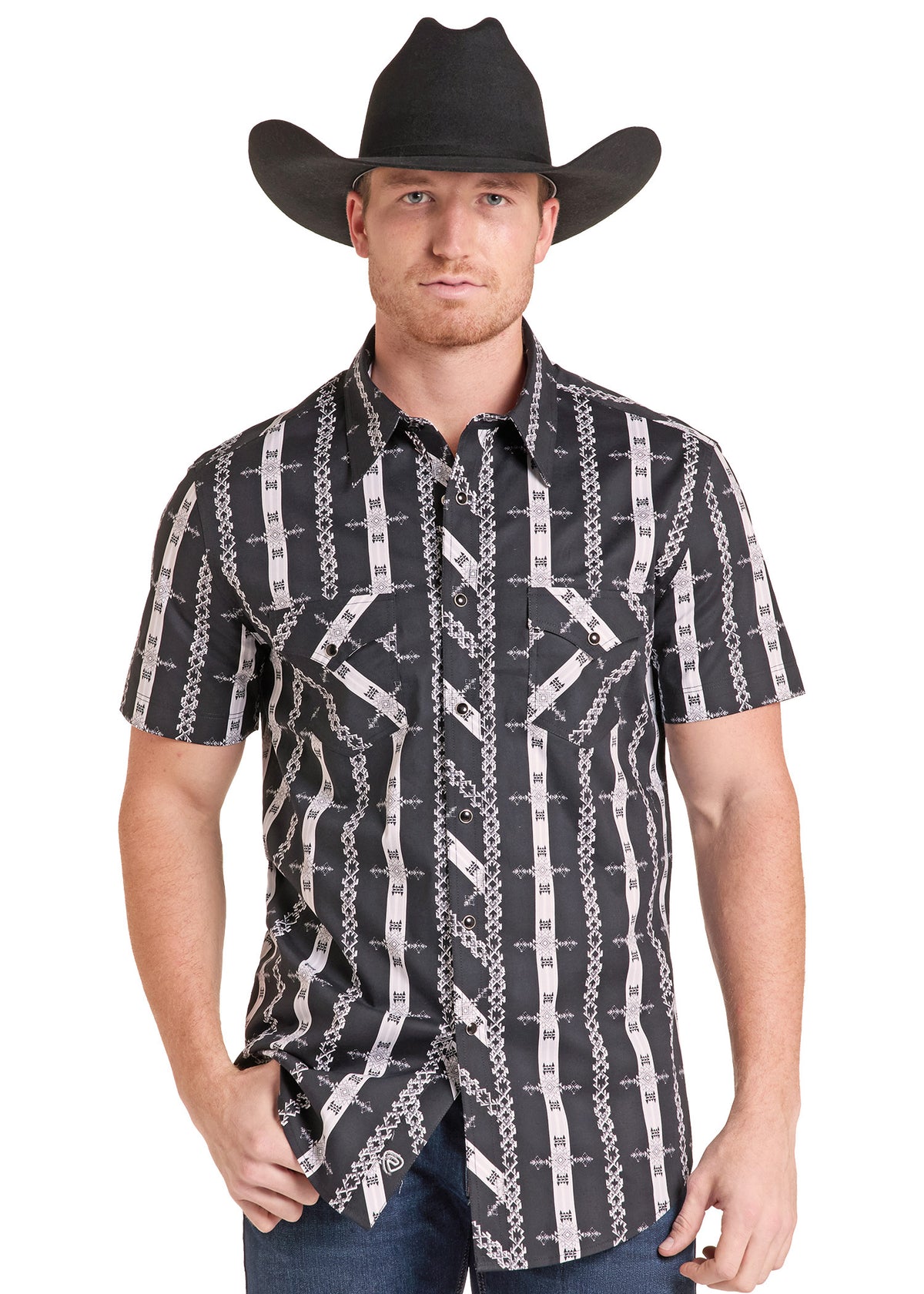 A man wearing a black and white western-style short-sleeve button-down shirt with a barbed wire and chain pattern, paired with a black cowboy hat and blue jeans, against a plain white background.