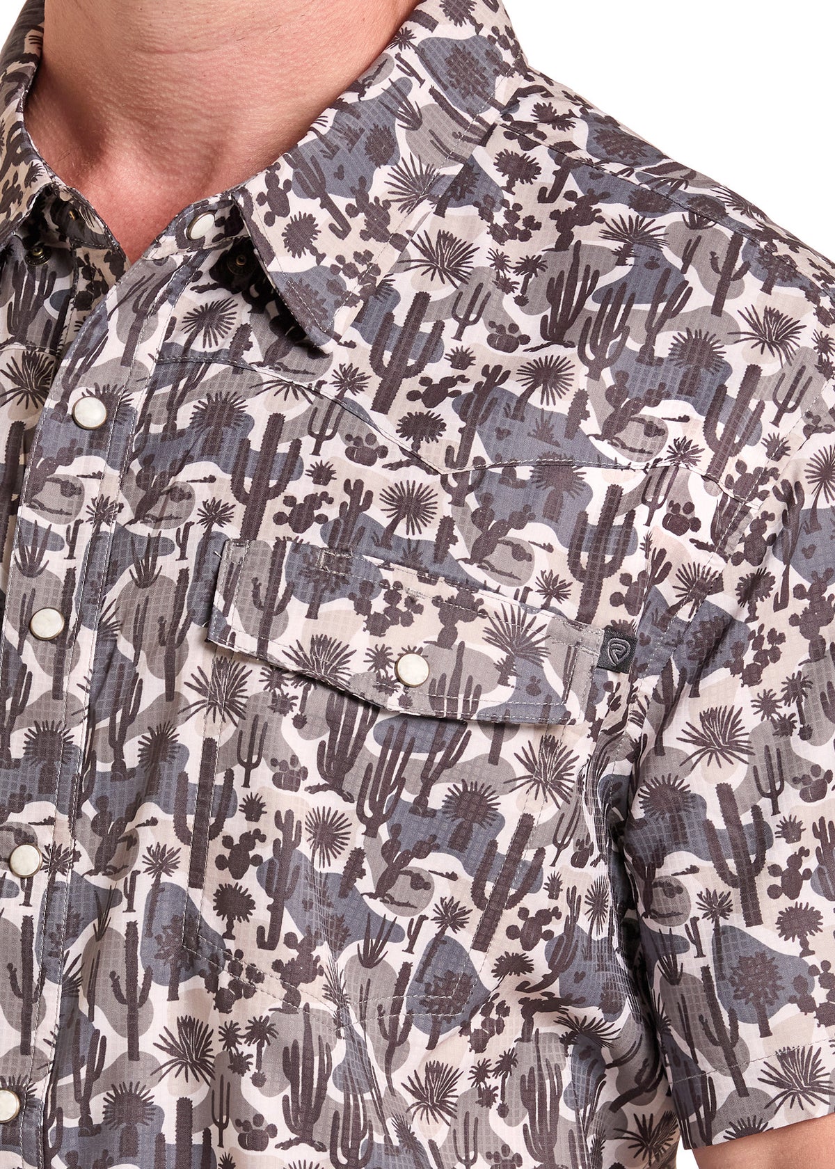Close-up of a short-sleeve button-up shirt with a desert cactus and succulent print in gray, brown, and off-white tones, worn by a model.