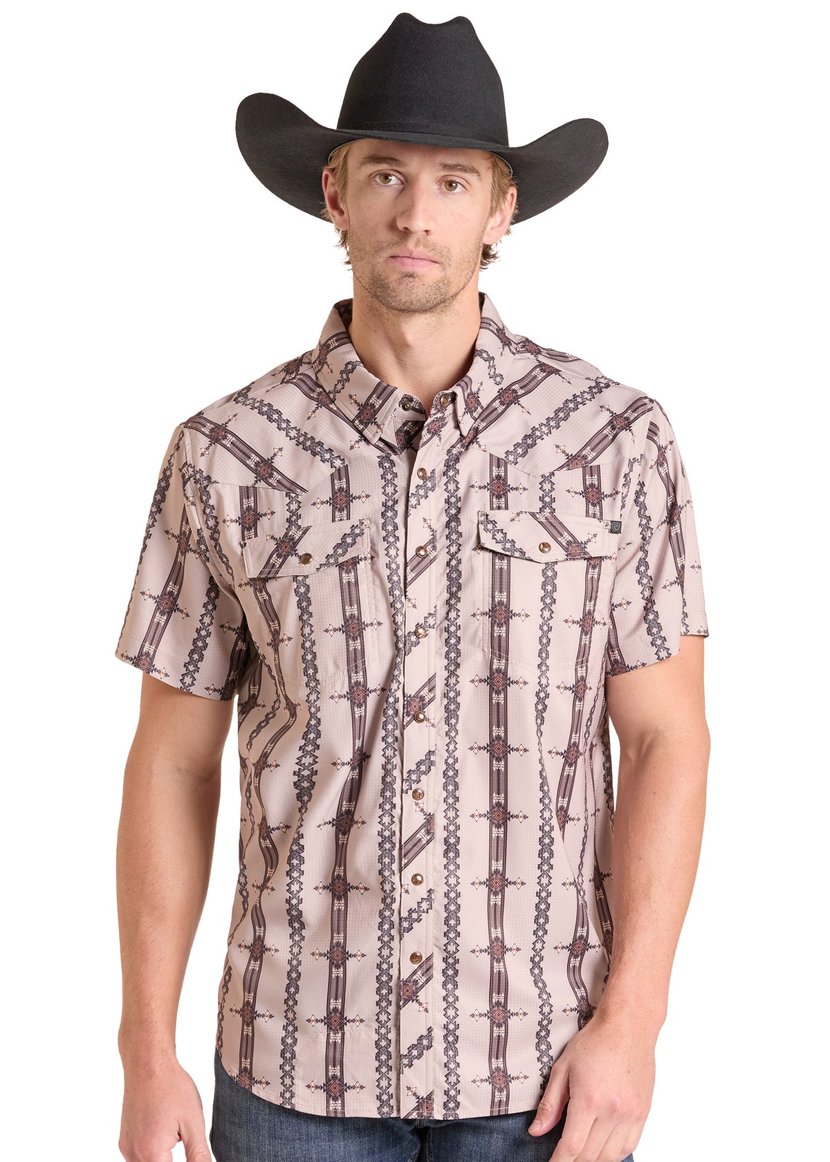 A man wearing a short-sleeve western button-up shirt with a brown and beige western-style geometric pattern, paired with a black cowboy hat and blue jeans, against a plain white background.
