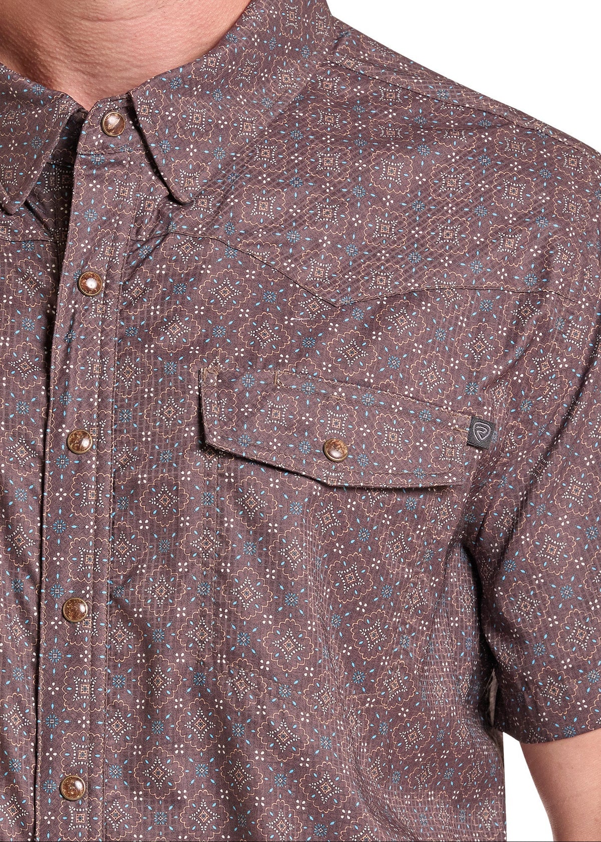 Close-up of a man wearing a short-sleeve button-up shirt with a brown, gray, and blue micro-pattern. The shirt features a pointed collar, a chest pocket with a snap button, and bronze-toned buttons.