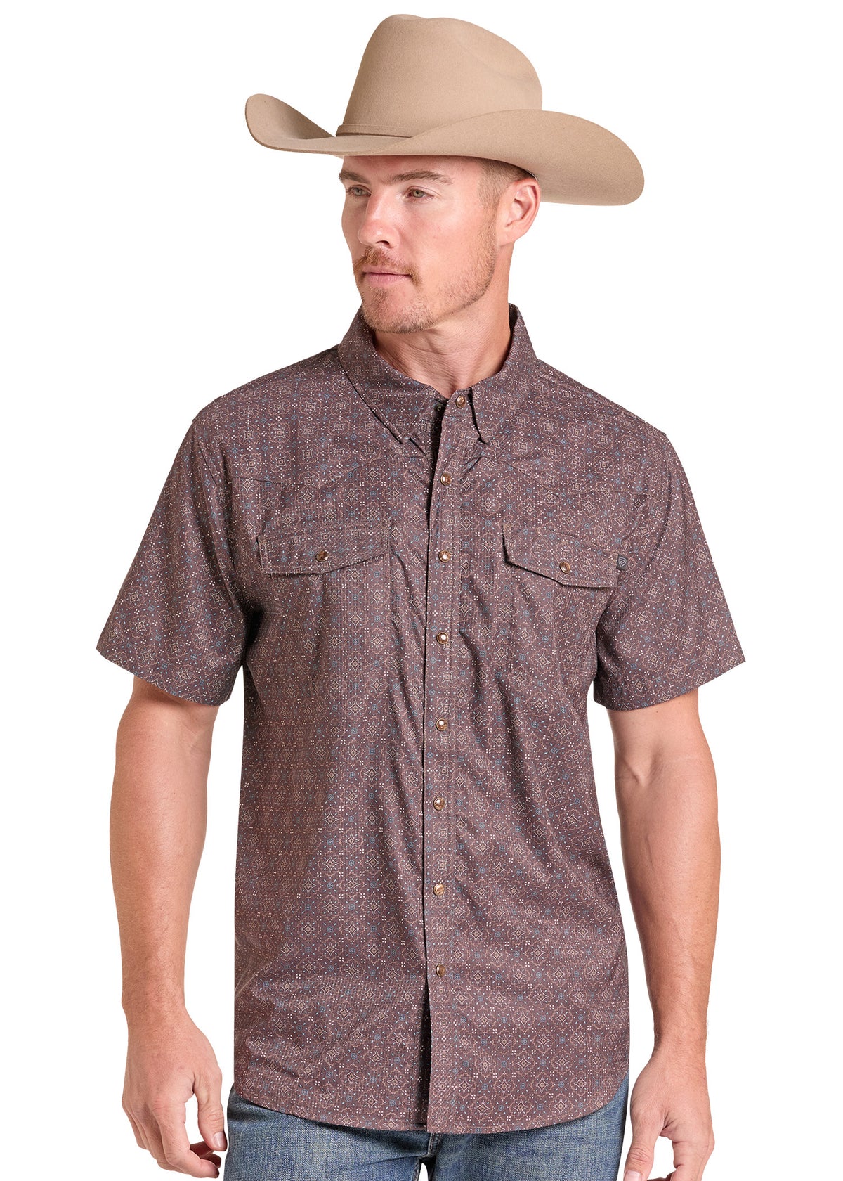 A man wearing a brown short-sleeve button-down shirt with a subtle geometric pattern, paired with a tan cowboy hat and blue jeans, shown against a plain white background.