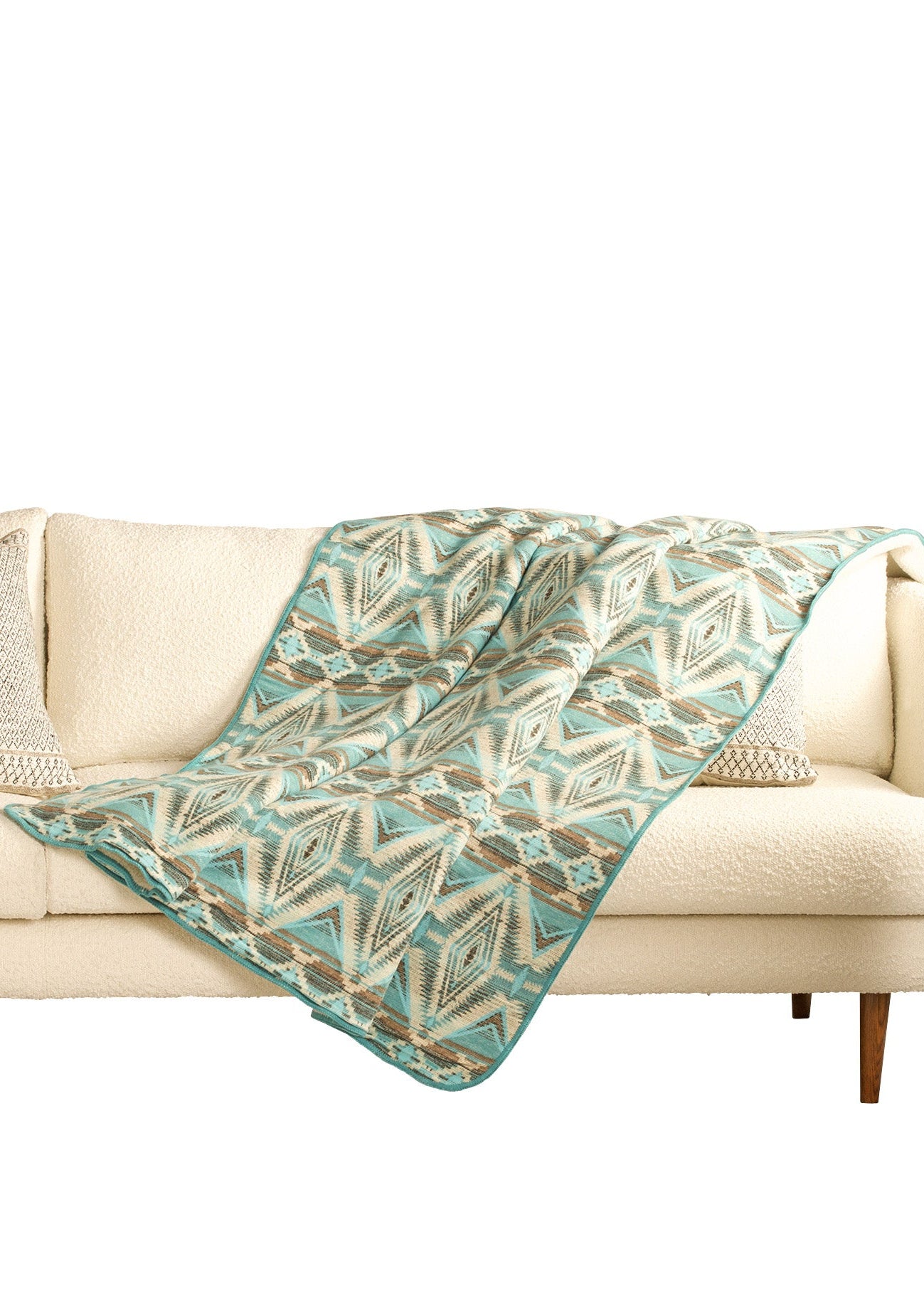 Teal and beige patterned throw blanket on a beige sofa against a white background