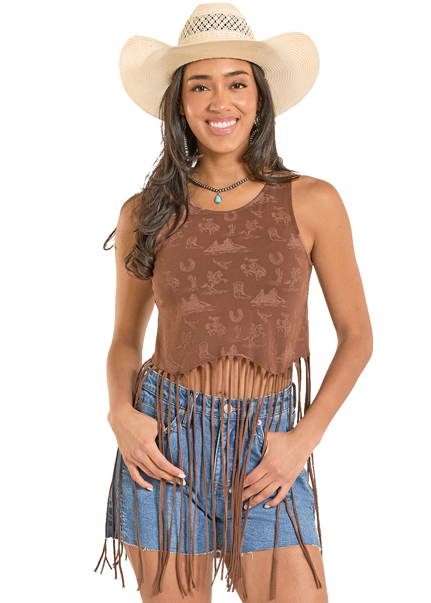 Woman wearing a brown patterned tank top with fringes and a blue denim shorts, paired with a beige cowboy hat on a white background.