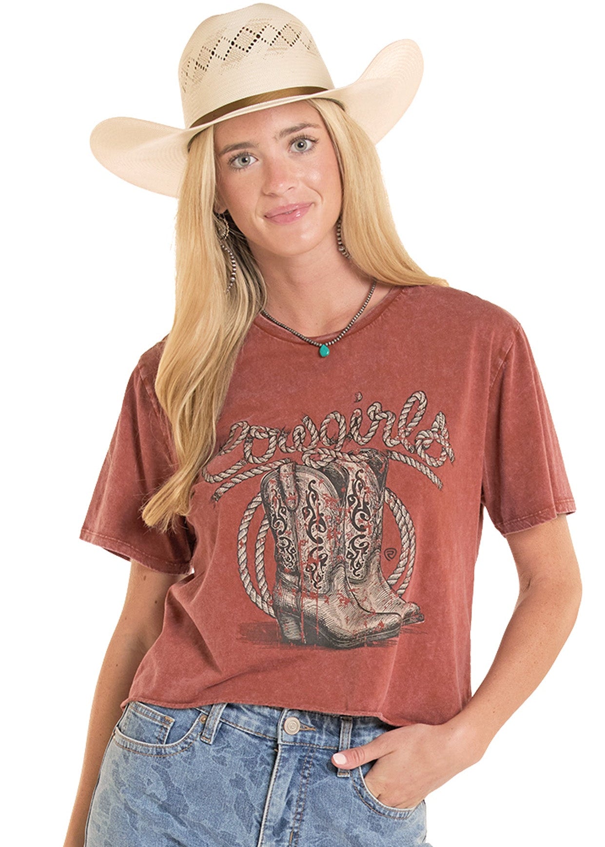 Woman wearing a red graphic t-shirt with a cowboy boot design, denim shorts, and a beige cowboy hat on a white background.
