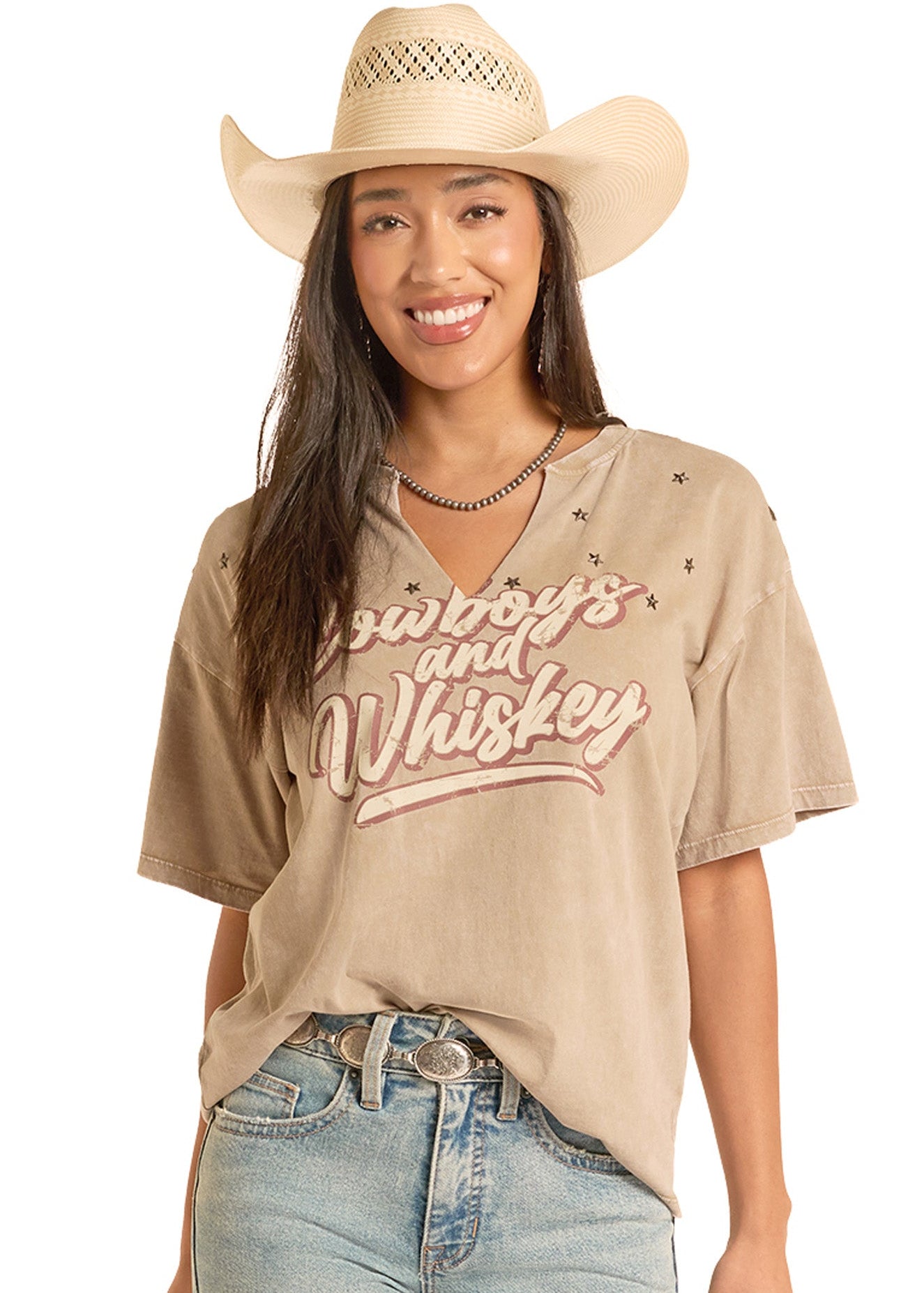 Woman wearing a beige 'Cowboys and Whiskey' shirt, light blue jeans, and a beige cowboy hat on a white background