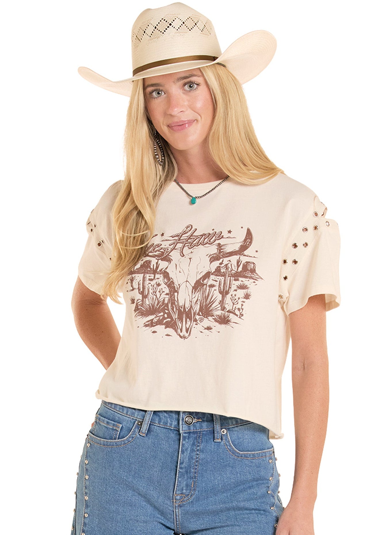 Woman wearing a cream t-shirt with graphic design and denim shorts, standing outdoors.