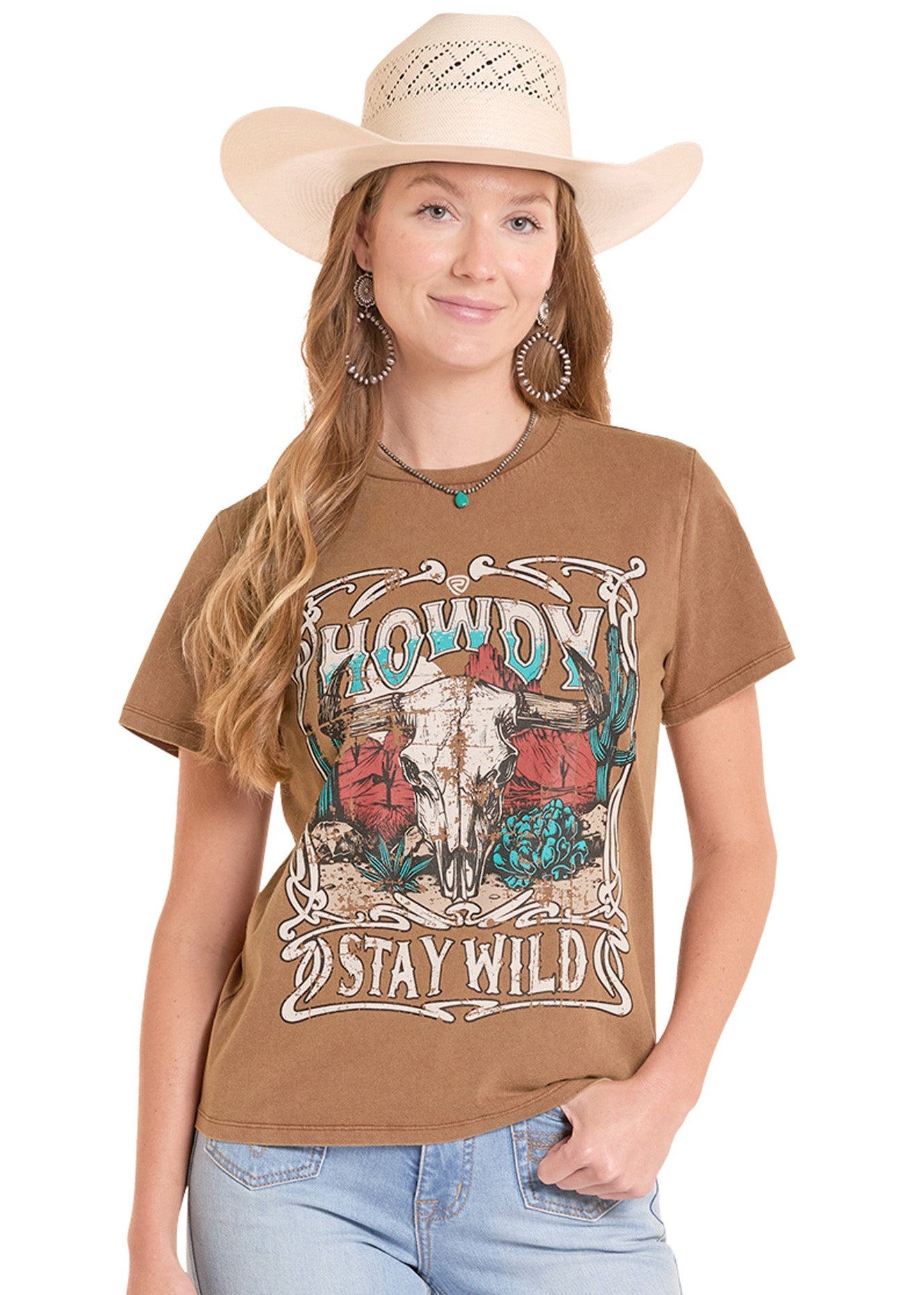 Woman wearing a brown graphic t-shirt with text and a cow skull design, paired with light blue jeans and a beige cowboy hat.