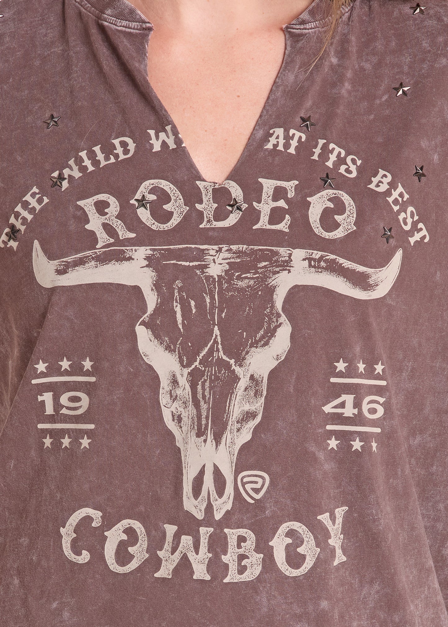 Close-up of a person wearing a brownish mauve V-neck t-shirt with a distressed white graphic of a longhorn skull and the words 'THE WILD WEST AT ITS BEST RODEO COWBOY'.