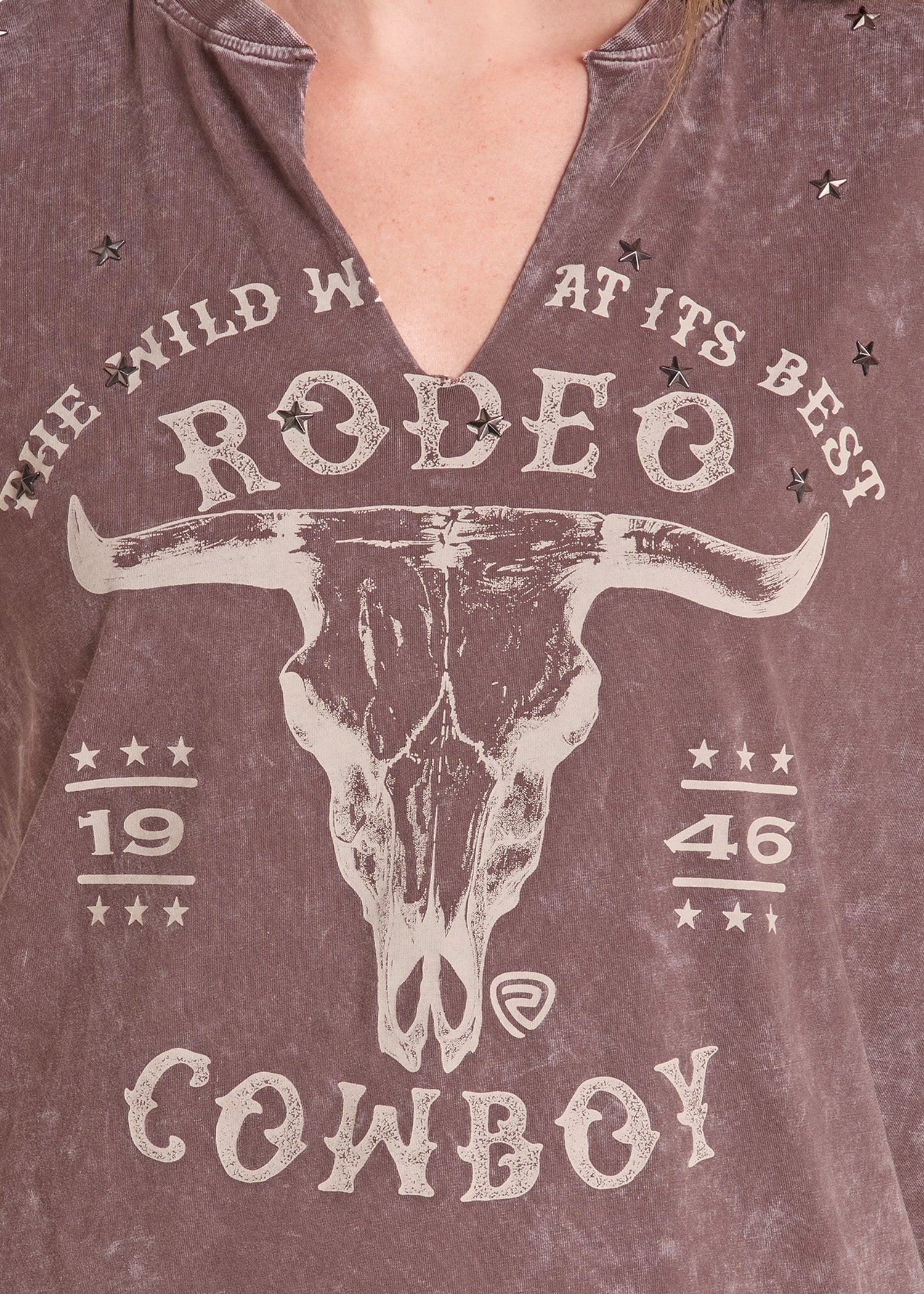 Close-up of a person wearing a brownish mauve V-neck t-shirt with a distressed white graphic of a longhorn skull and the words 'THE WILD WEST AT ITS BEST RODEO COWBOY'.