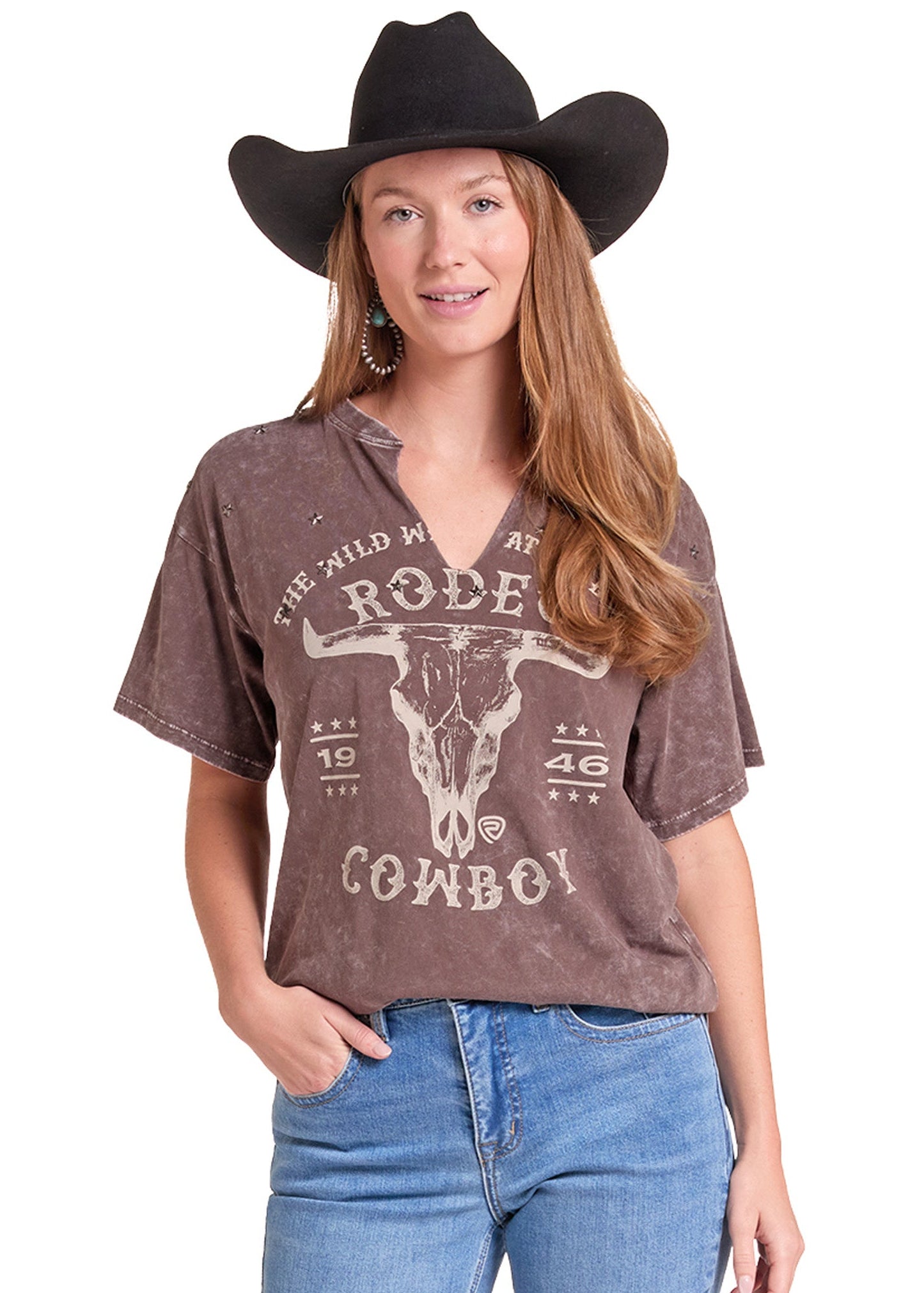 A woman modeling a brown acid-wash graphic t-shirt with a distressed cow skull and 'The Wild West Rodeo Cowboy' print, paired with blue jeans.