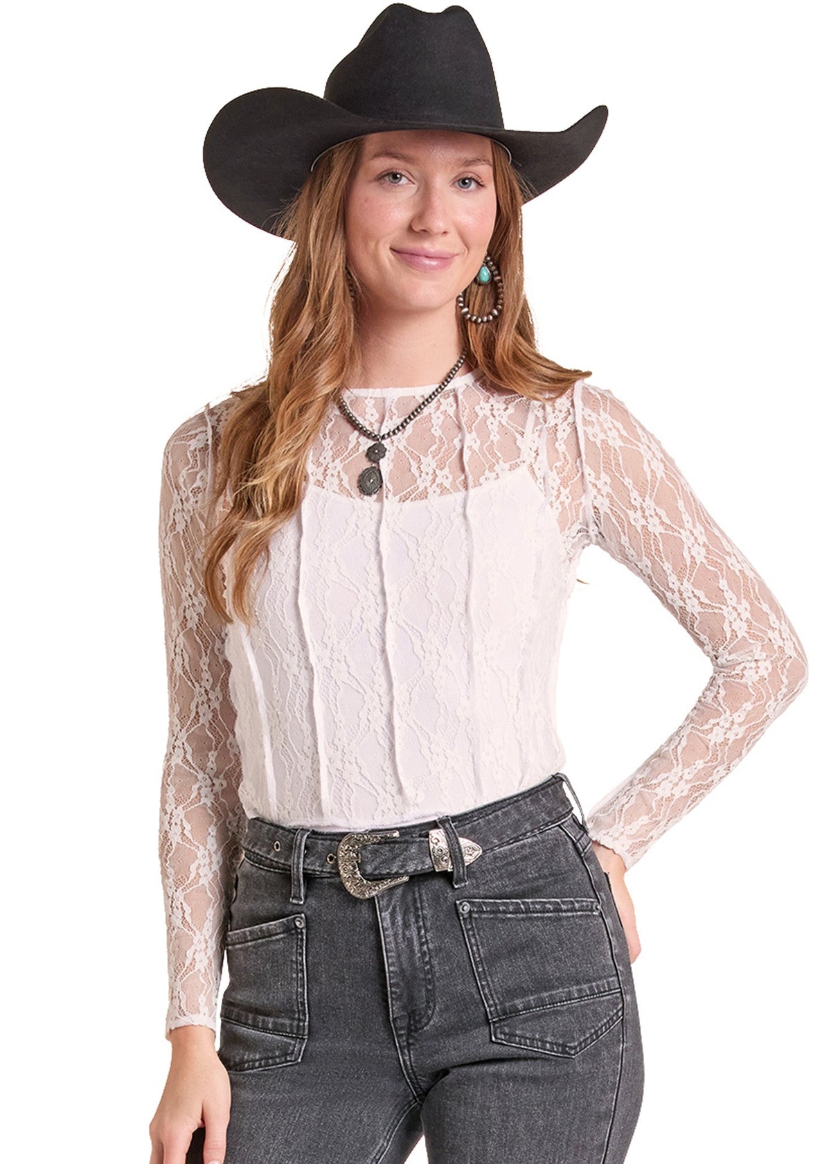 A woman modeling a white lace long-sleeve top with a pleated front, paired with dark gray jeans, a black cowboy hat, and a silver necklace, against a plain white background.