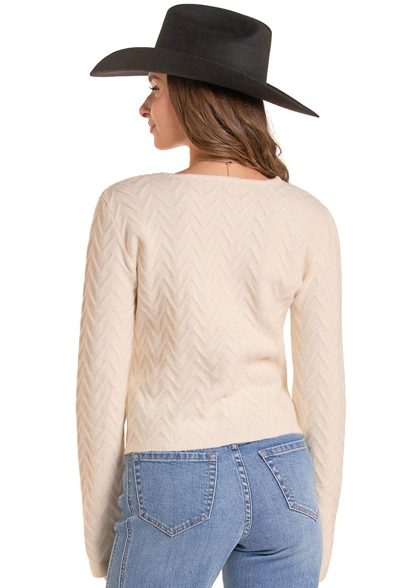 A woman shown from the back wearing a cream cable-knit sweater, light blue straight-leg jeans, and a black cowboy hat against a plain white background.