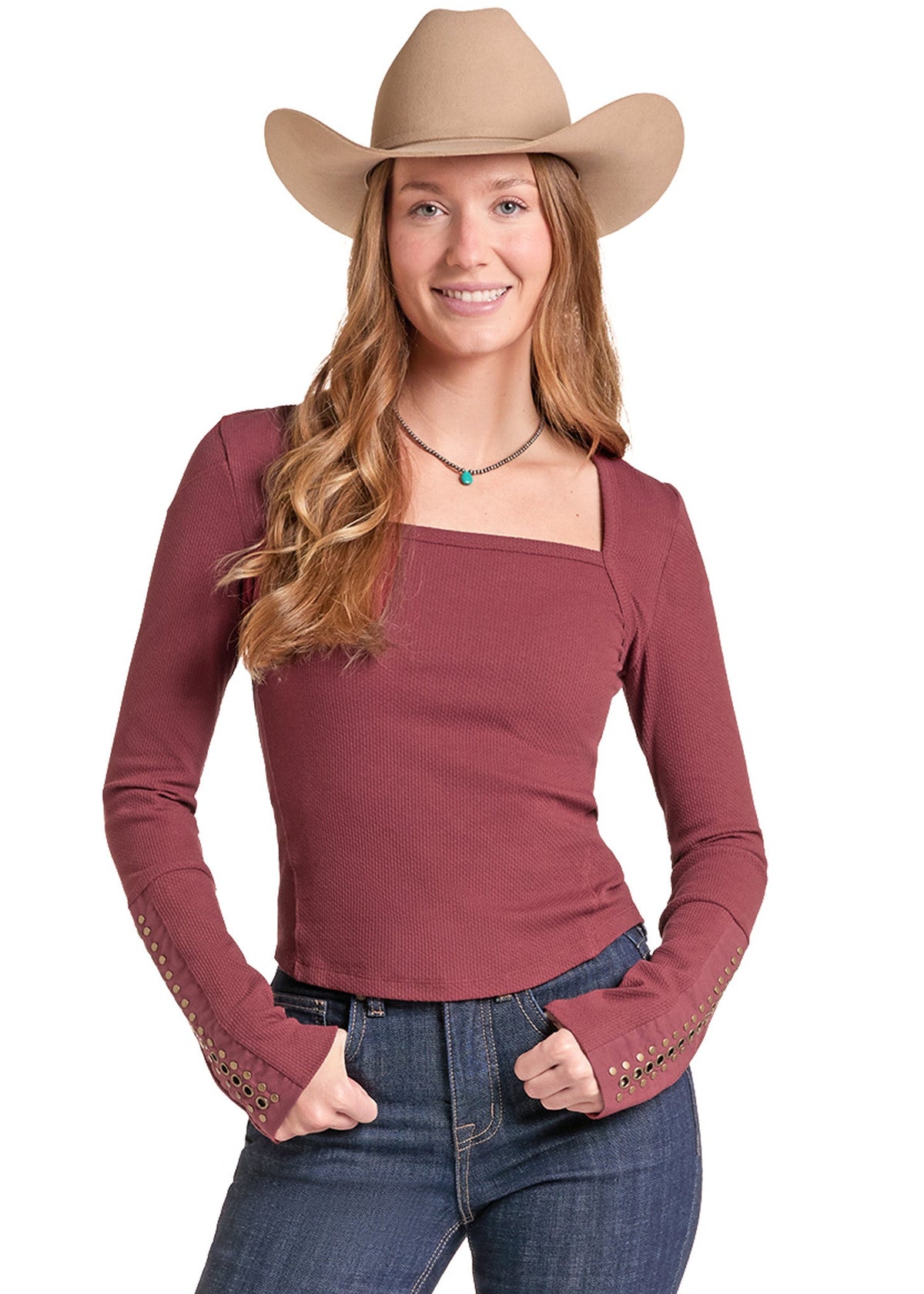 A woman modeling a long-sleeve scoop-neck top in dusty rose, paired with blue jeans and a tan cowboy hat, against a plain white background.
