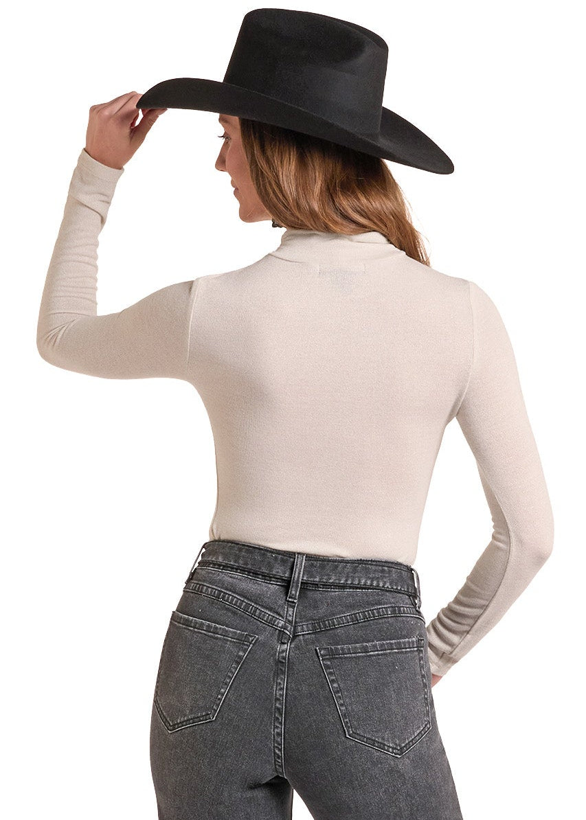 A woman shown from the back wearing a black wide-brim cowboy hat, a fitted cream long-sleeve top, and high-waisted dark gray flare jeans against a plain white background.