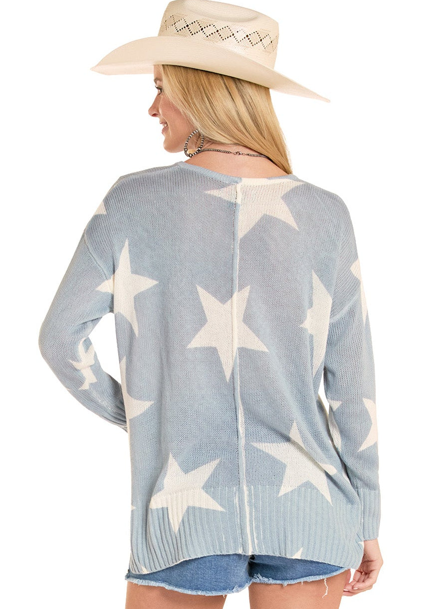 Woman wearing a light blue sweater with star patterns, denim shorts, and white cowboy boots on a white background.