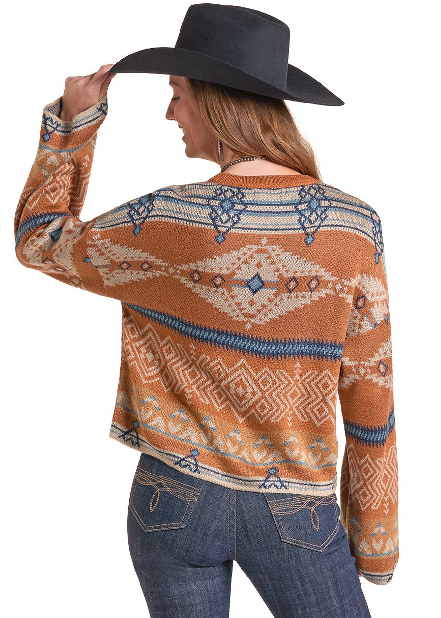 A woman shown from the back wearing a rust-orange cropped knit sweater with a blue and cream geometric pattern, blue jeans, and a black cowboy hat against a white background.