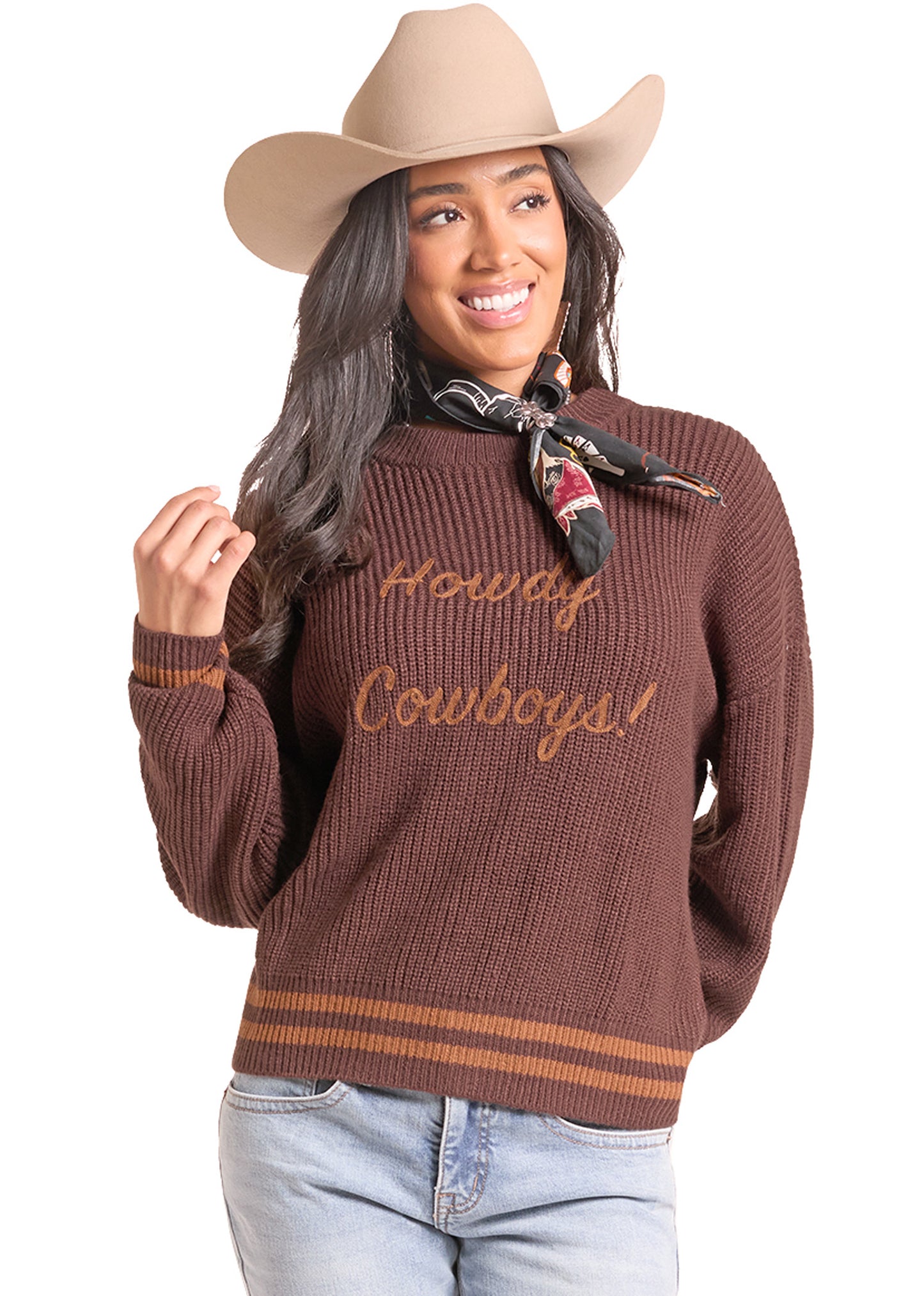 A woman wearing a brown ribbed knit sweater with 'Howdy Cowboys!' embroidered in tan across the chest, styled with a tan cowboy hat,