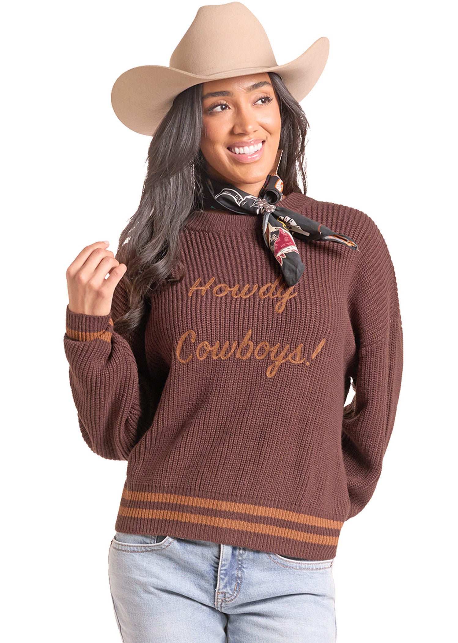 A woman wearing a brown ribbed knit sweater with 'Howdy Cowboys!' embroidered in tan across the chest, styled with a tan cowboy hat,